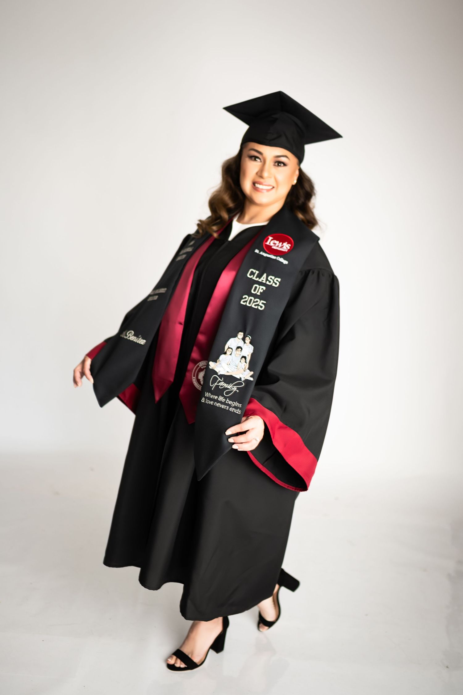 Graduate poses in black academic regalia with red trim against white background.