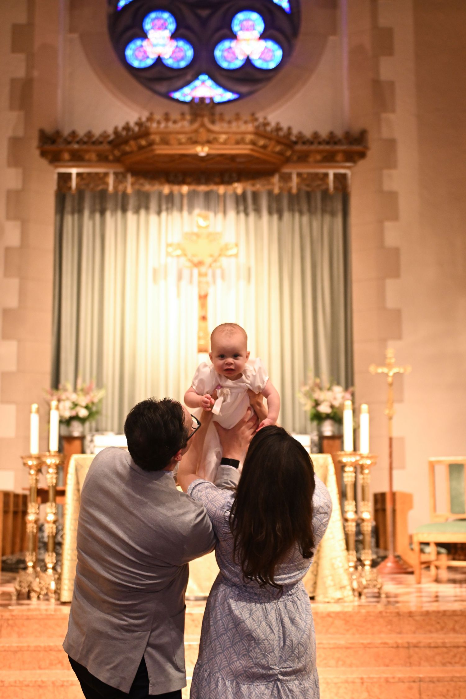 A baptism ceremony taking place in a church with stained glass windows and an ornate altar.