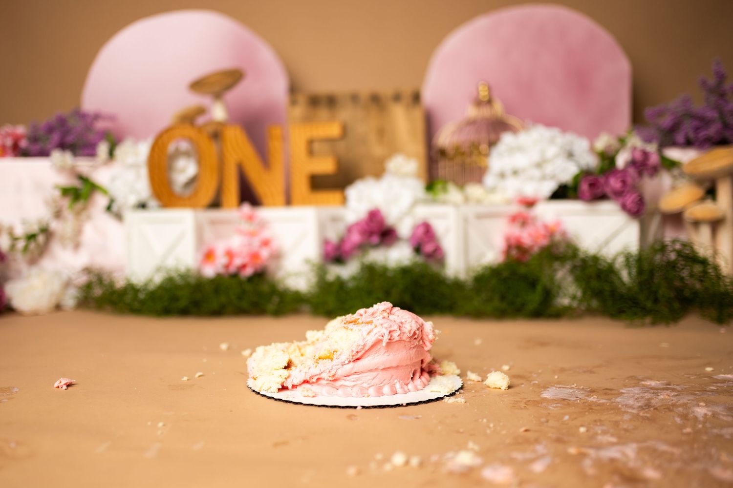 Smashed pink birthday cake on wooden stand during first birthday photoshoot.