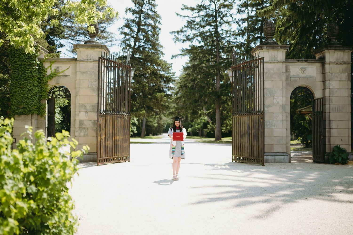 Person walking through grand stone gateway entrance on sunny campus path.