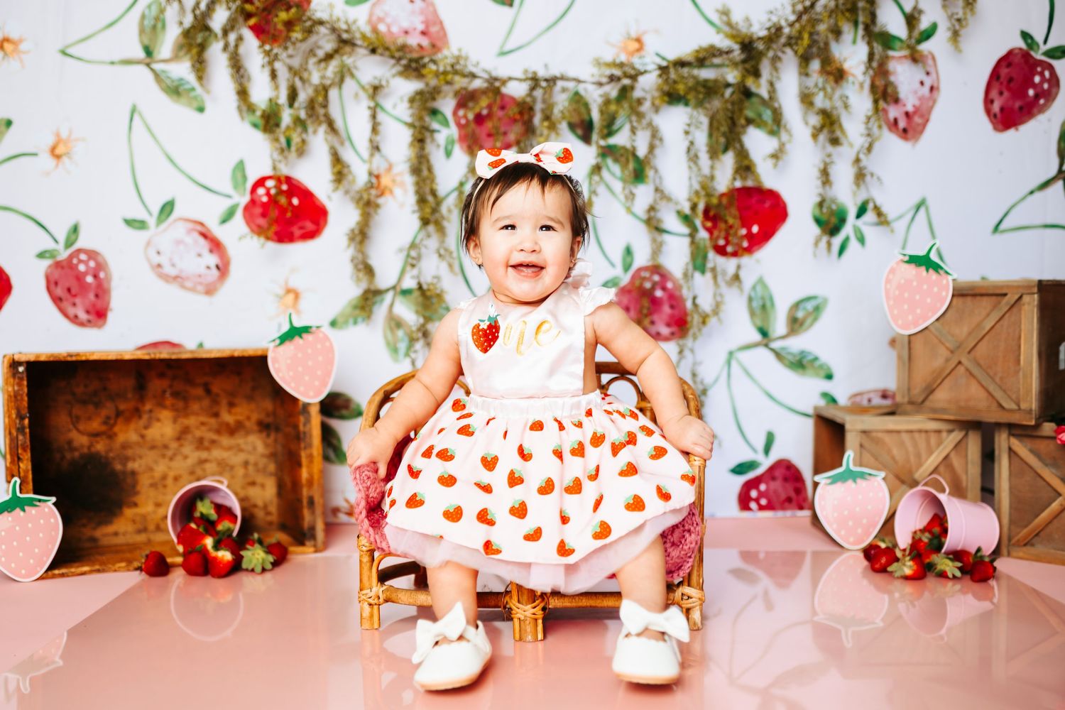 First birthday celebration setup with strawberry pattern backdrop and pink decorations.