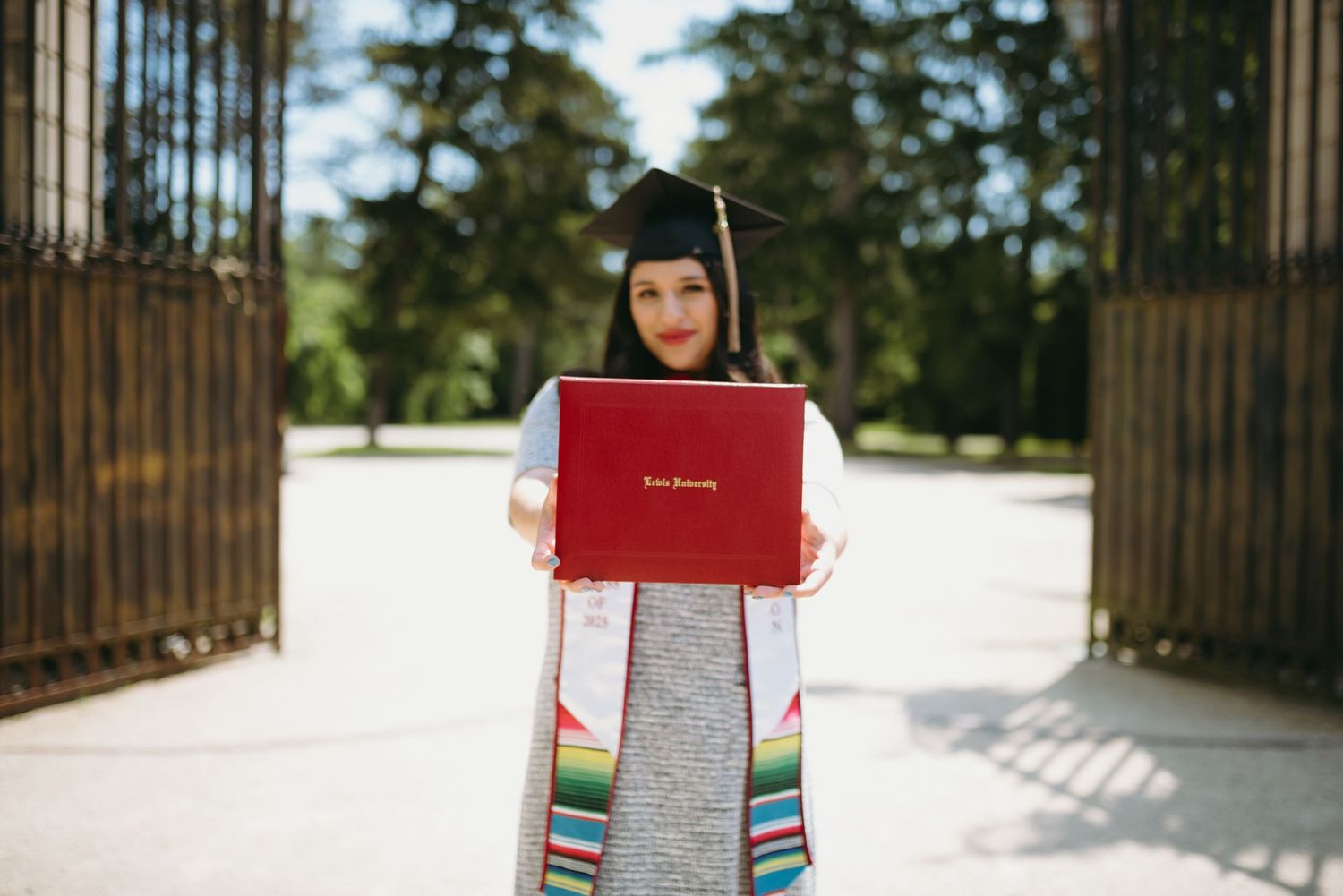 Graduate holds diploma while standing in snowy winter landscape with evergreen trees.