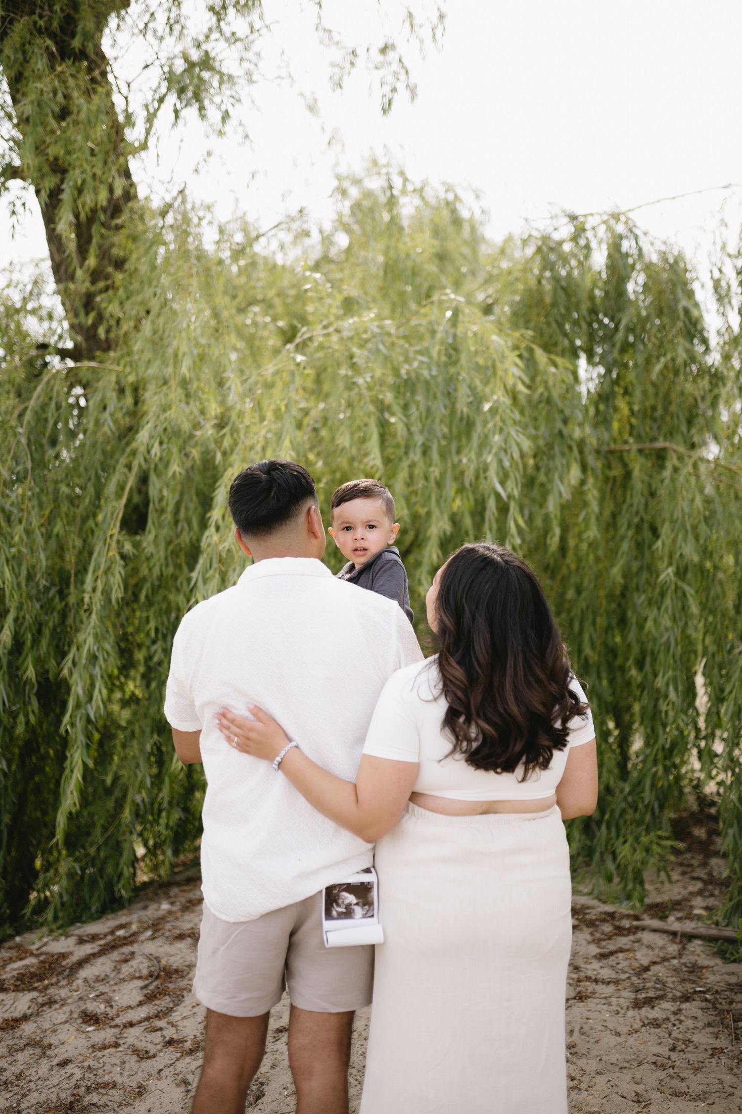 A family wearing coordinated white outfits poses together near willow trees.