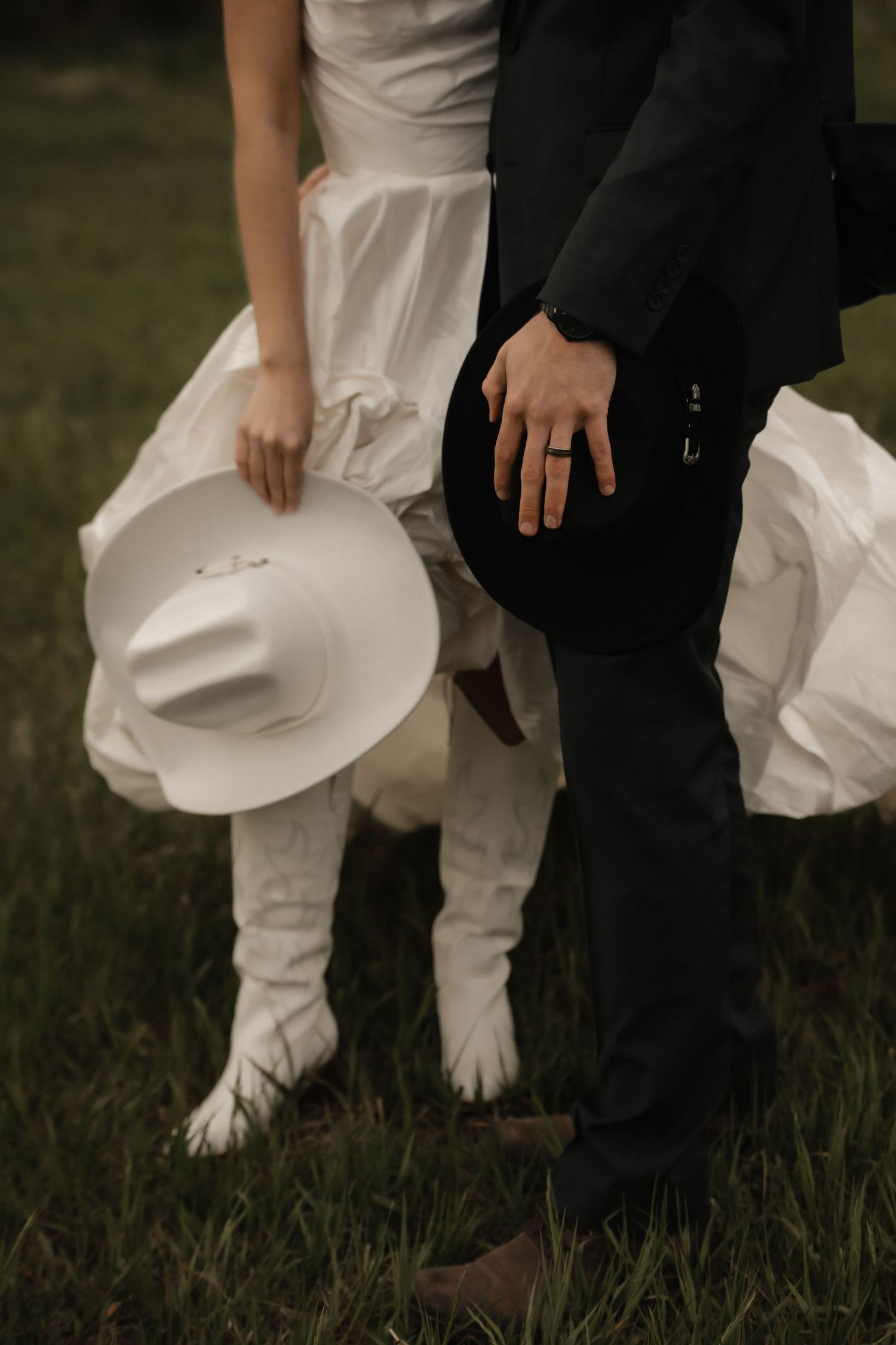 A close-up view of formal shoes and white wedding dress hem on grassy ground during an outdoor wedding ceremony.