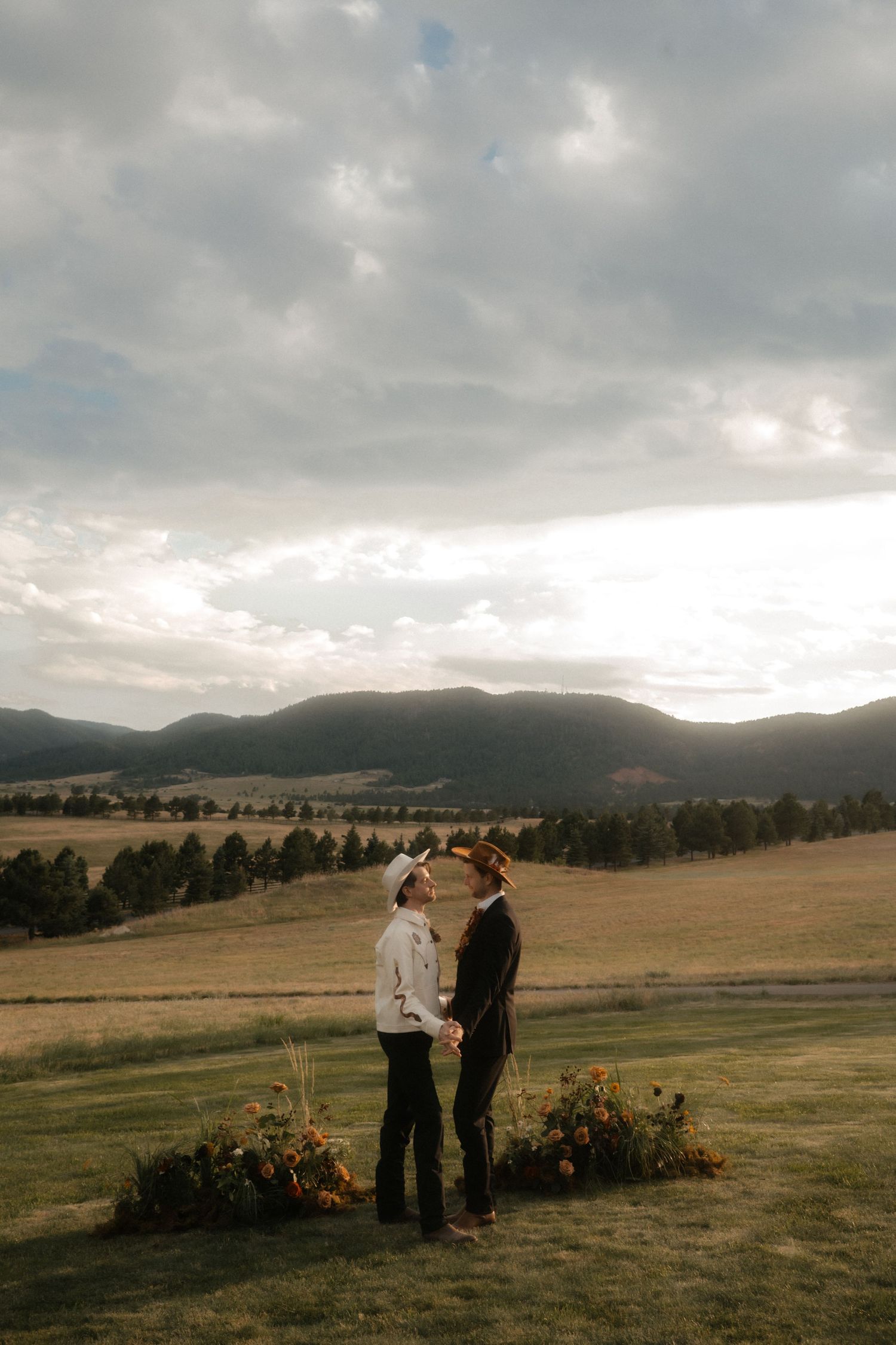 Couple stands in an open field with mountains and dramatic cloudy sky in the background during an intimate ceremony.
