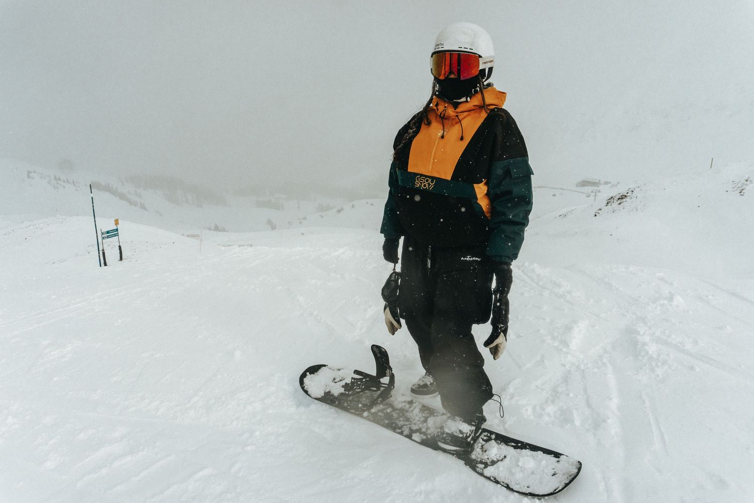 A snowboarder glides down a snowy slope in an orange and black winter jacket against a white winter landscape.