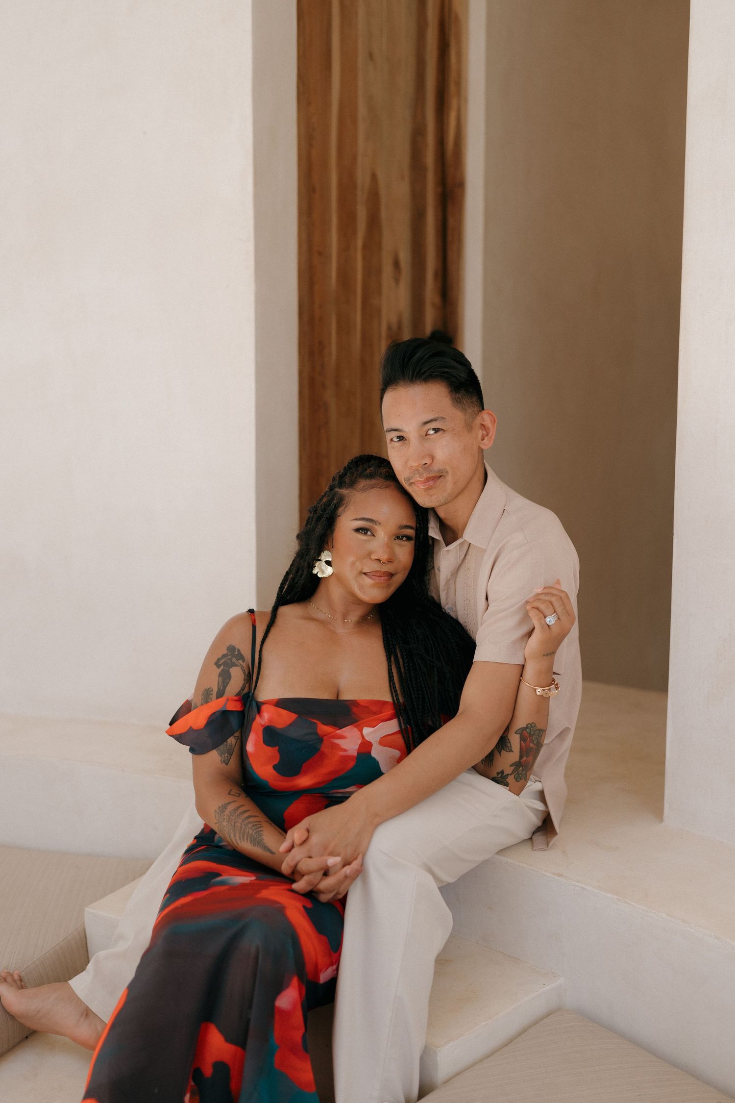 A couple in casual attire lounges together in a minimalist interior with white walls and warm lighting.
