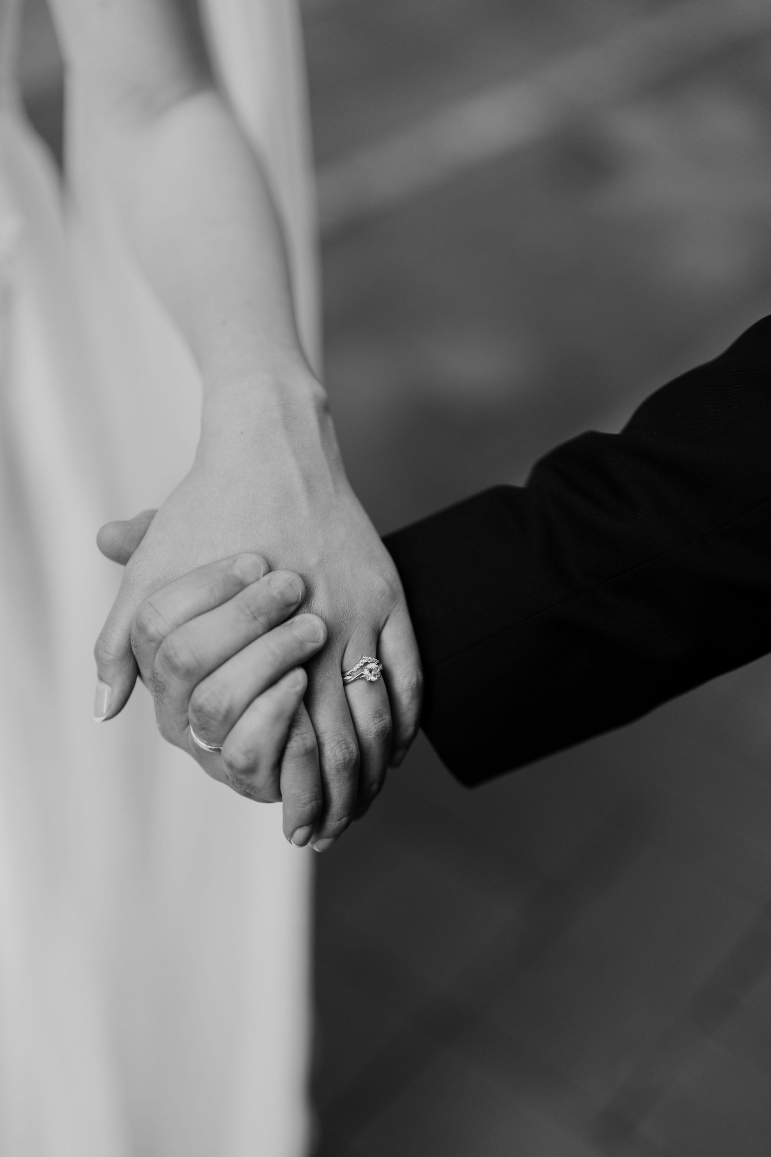 Black and white close-up of newlyweds holding hands showing engagement ring.