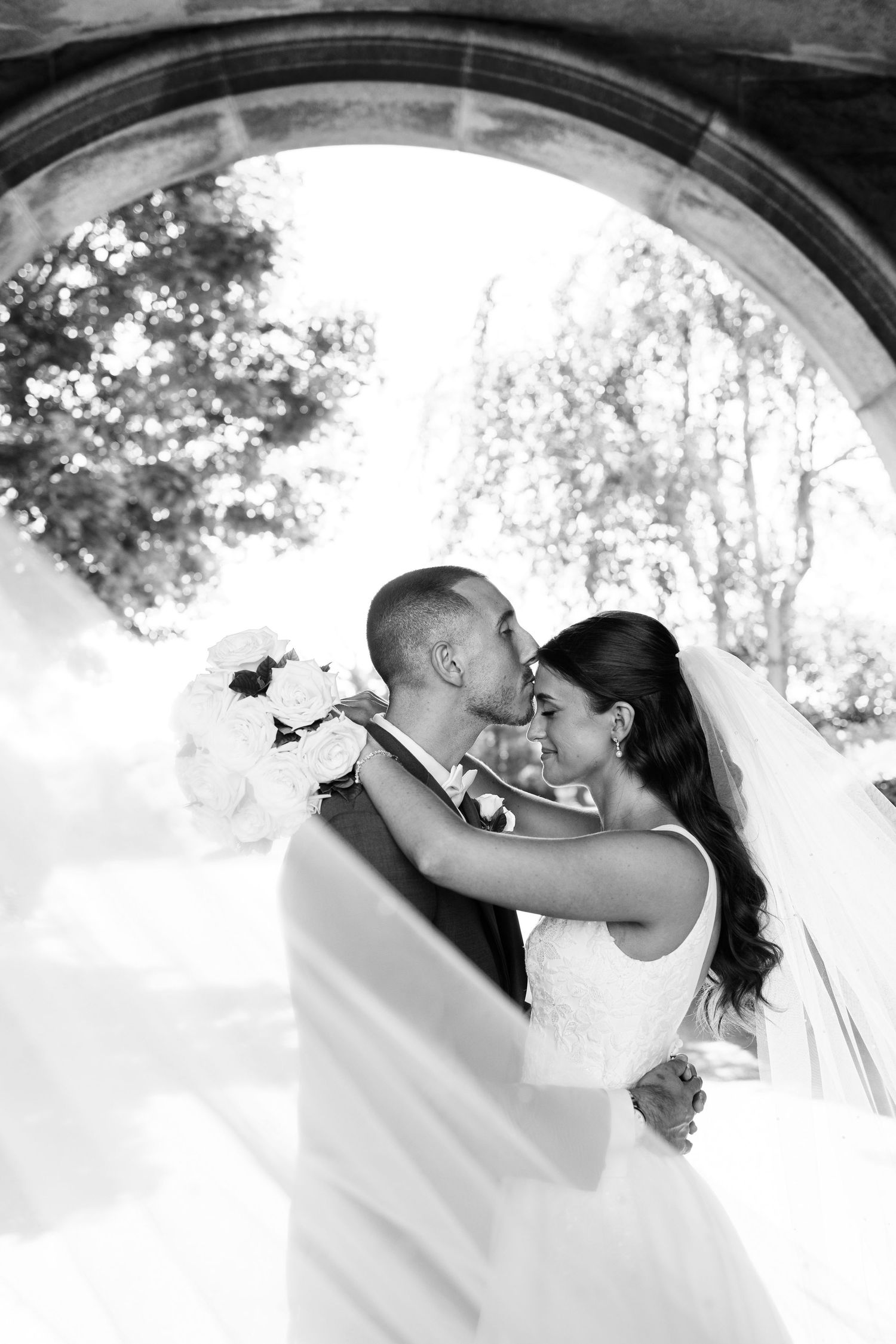 Romantic wedding kiss sequence under stone archway with natural lighting.