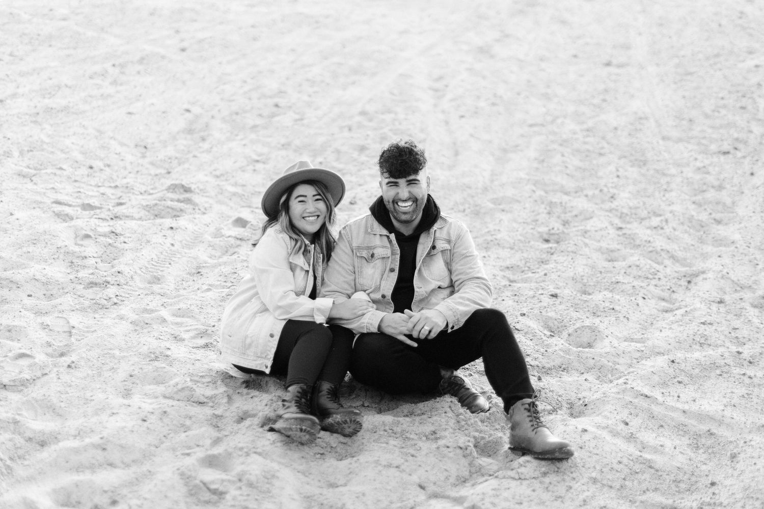 Couple in light denim outfits shares playful moments on sandy beach together.