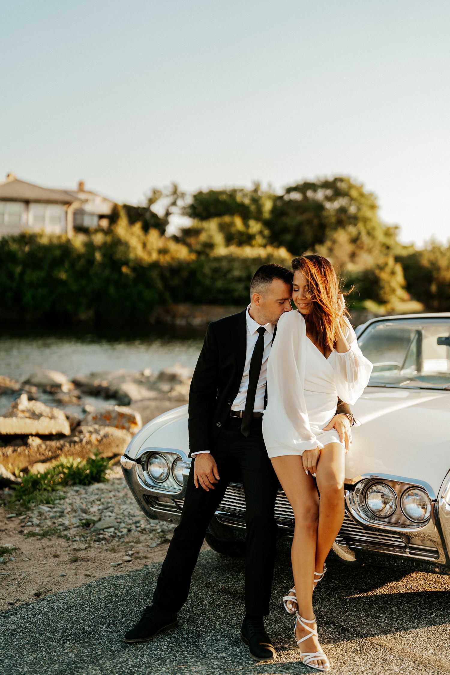 Romantic couple poses by vintage car during golden hour photoshoot.