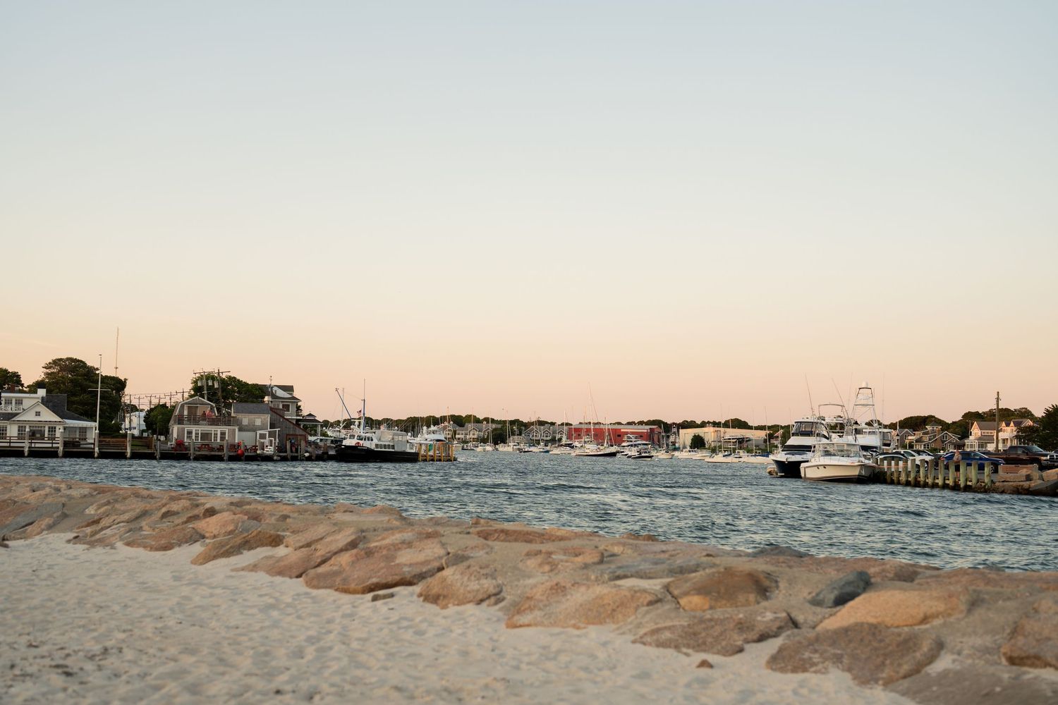 Panoramic view of a coastal harbor town with boats and buildings along the waterfront at sunset.