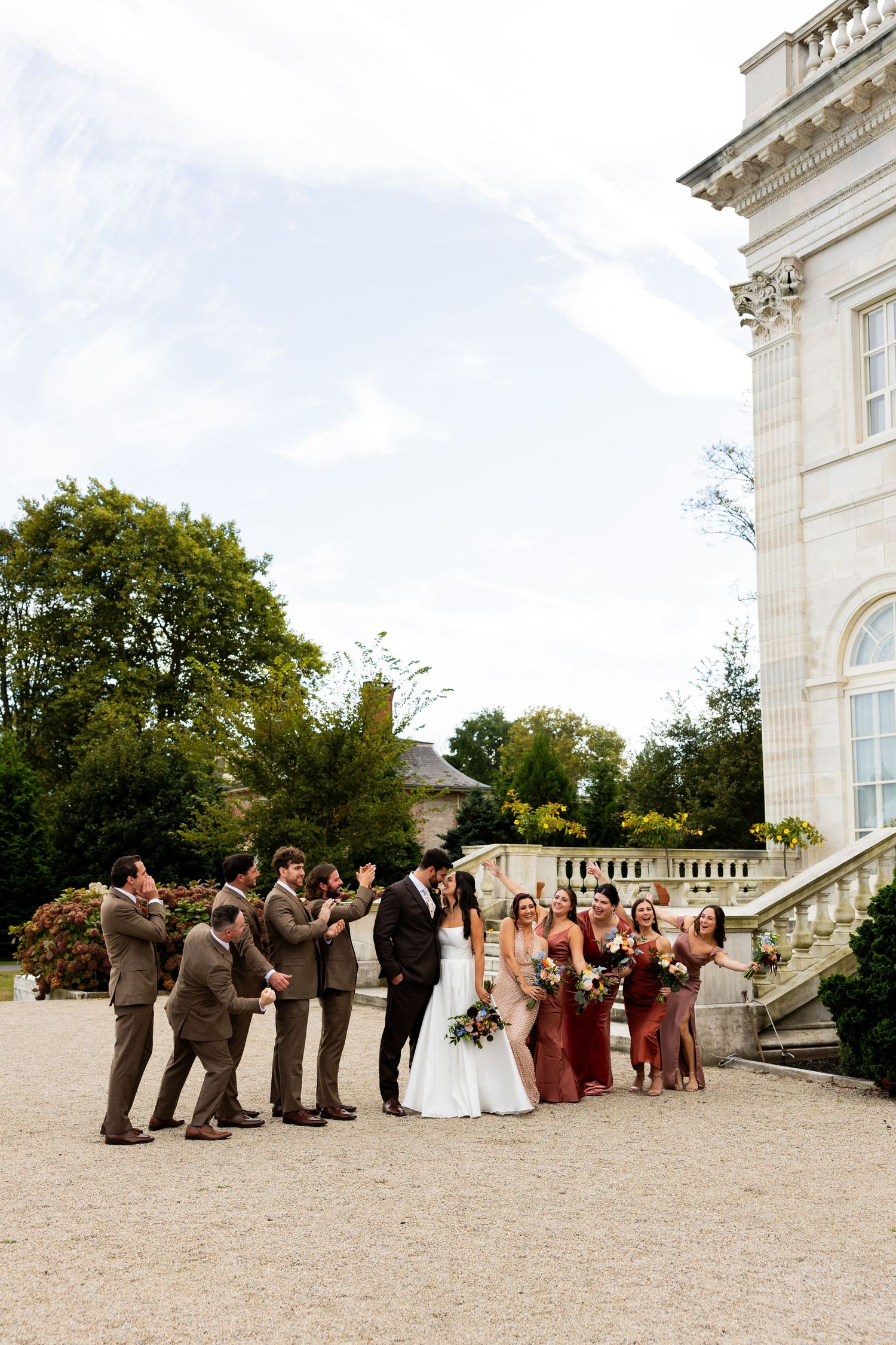 Wedding party members pose together on the grounds of an elegant white estate.