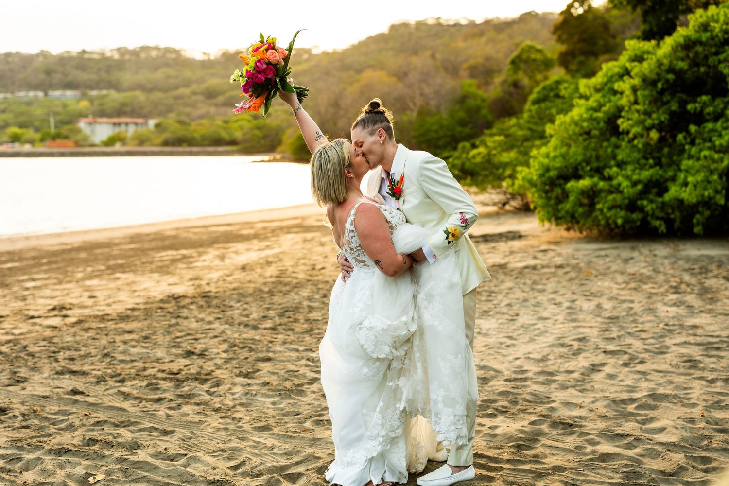 A couple celebrates their beach wedding during golden hour with vibrant flowers.