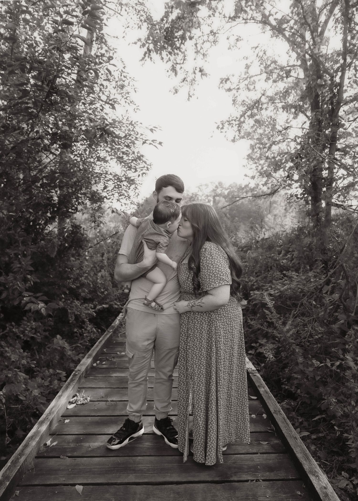 Black and white family photo with baby boy giving mom kisses in dad's arms