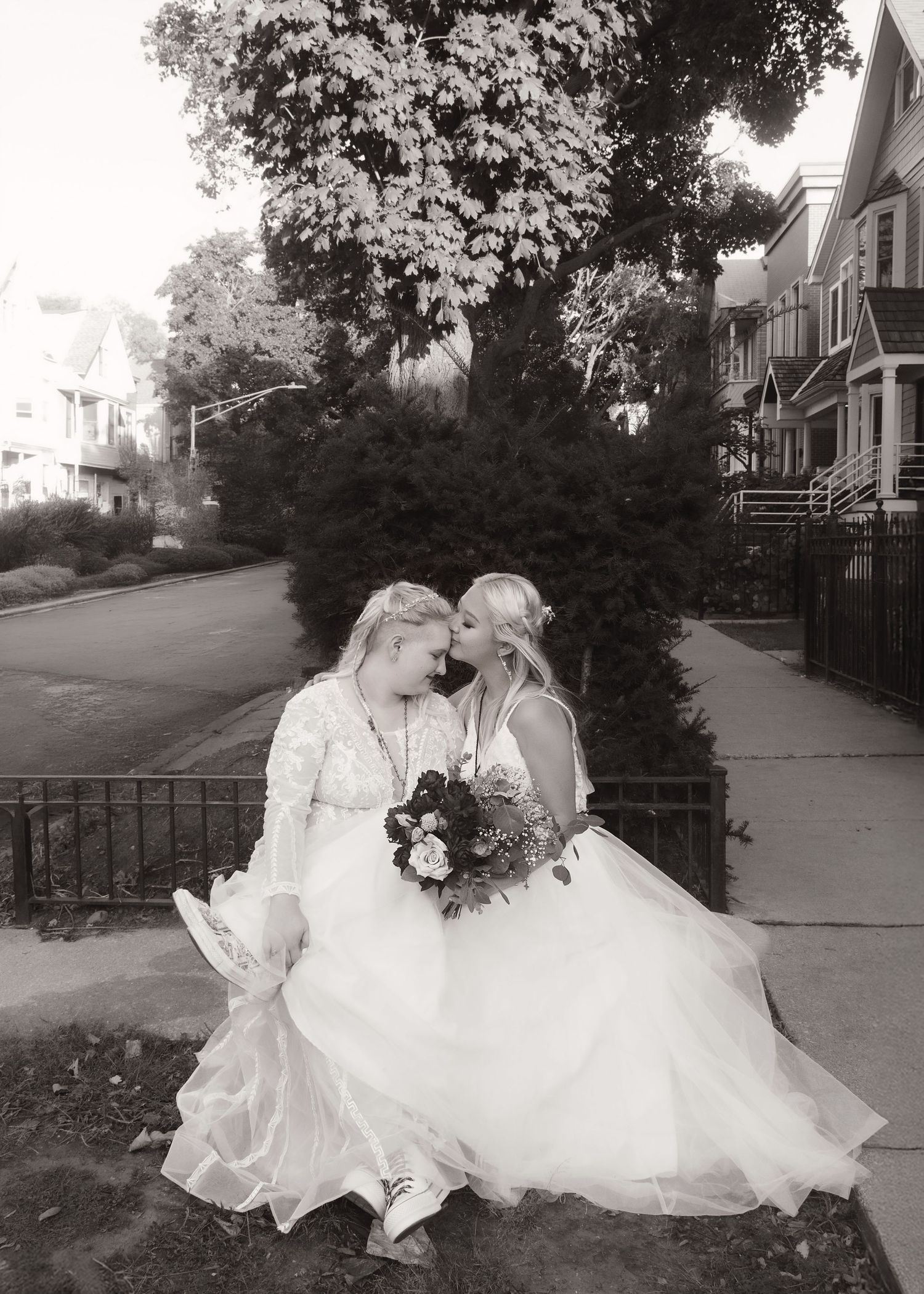 Lovely lesbian couple photo during wedding with comfortable shoes and flowy dresses, snuggling up on a bench outside their home