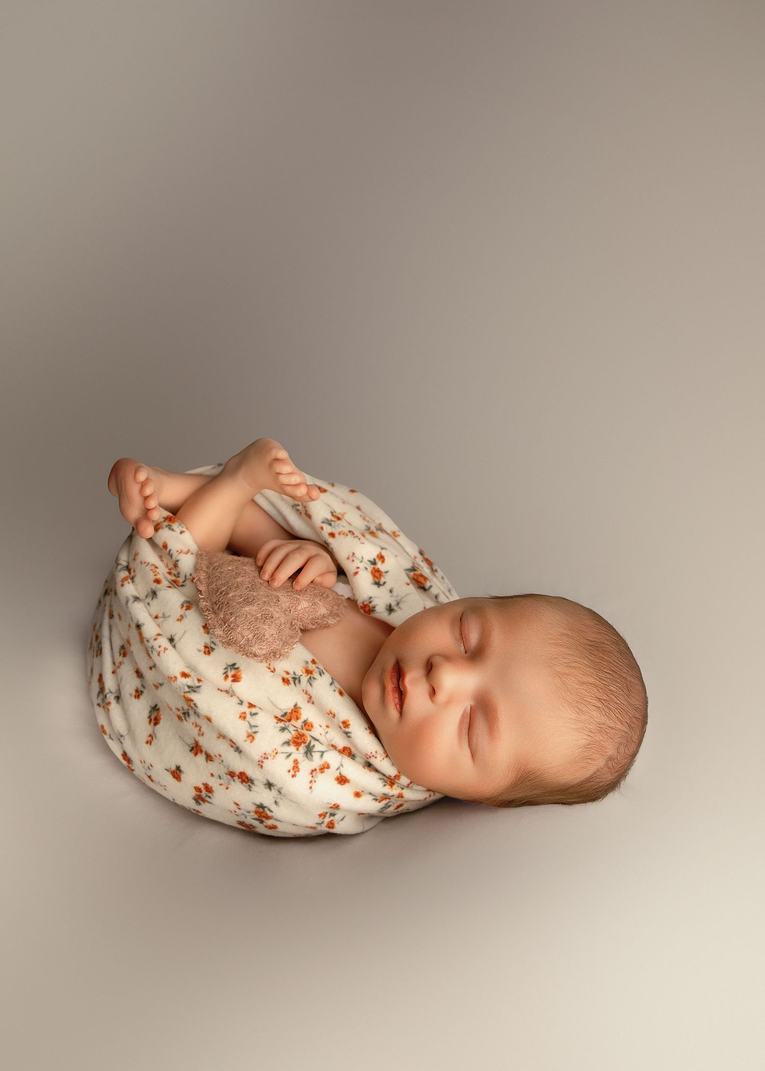Newborn baby girl posed in studio with flowered wrap and plush heart in Peoria, IL