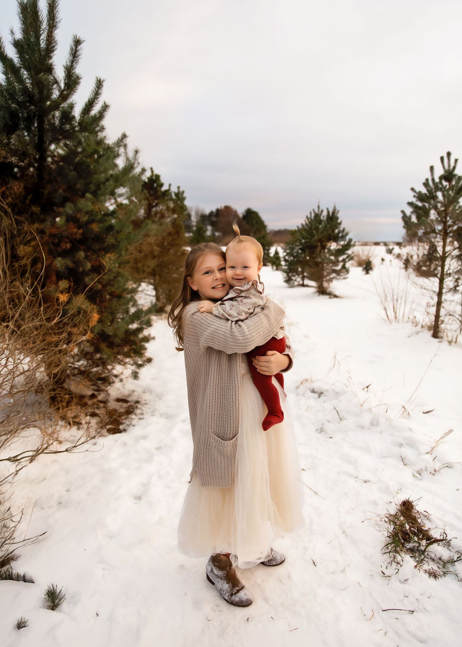 Christmas tree farm family session with baby girl and her big sister snuggling in the snow