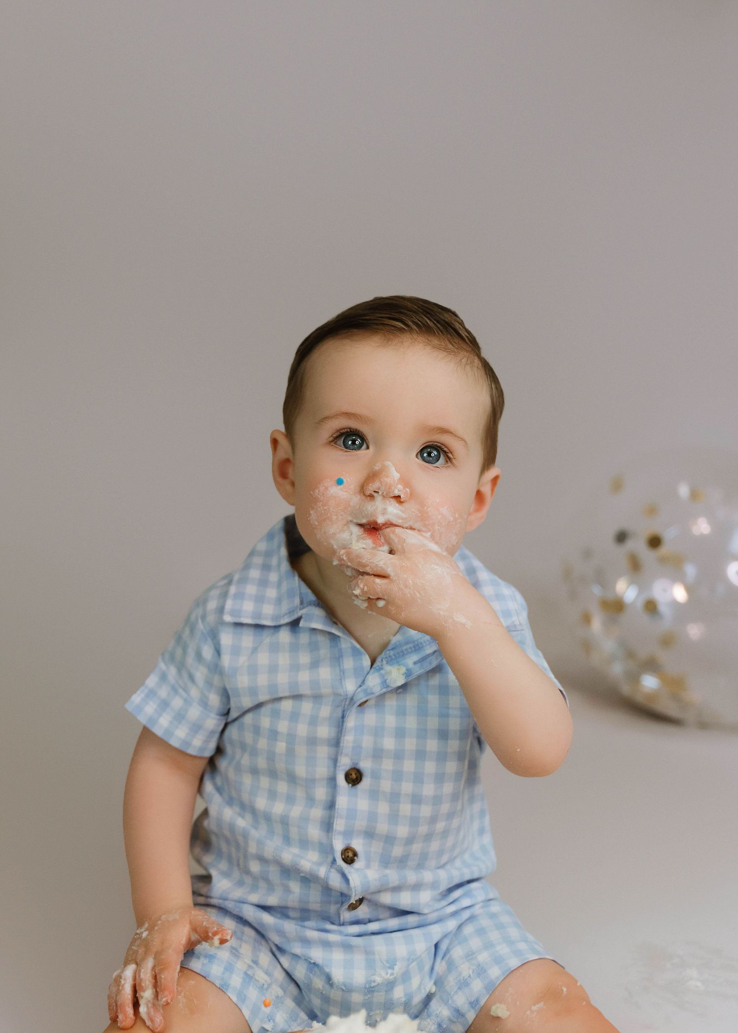 Close up portrait of in-studio boy cake smash session with balloons and cake all over the face