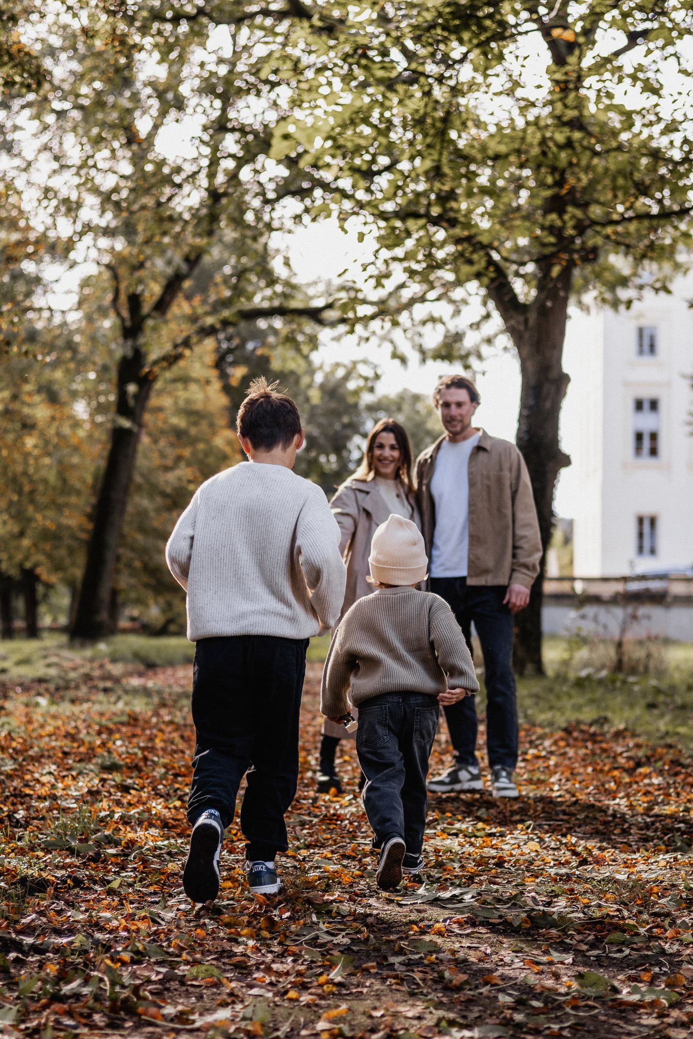 Familie spaziert gemeinsam durch einen Park, bedeckt mit gefallenem Herbstlaub und den letzten Sonnenstrahlen in Trier.