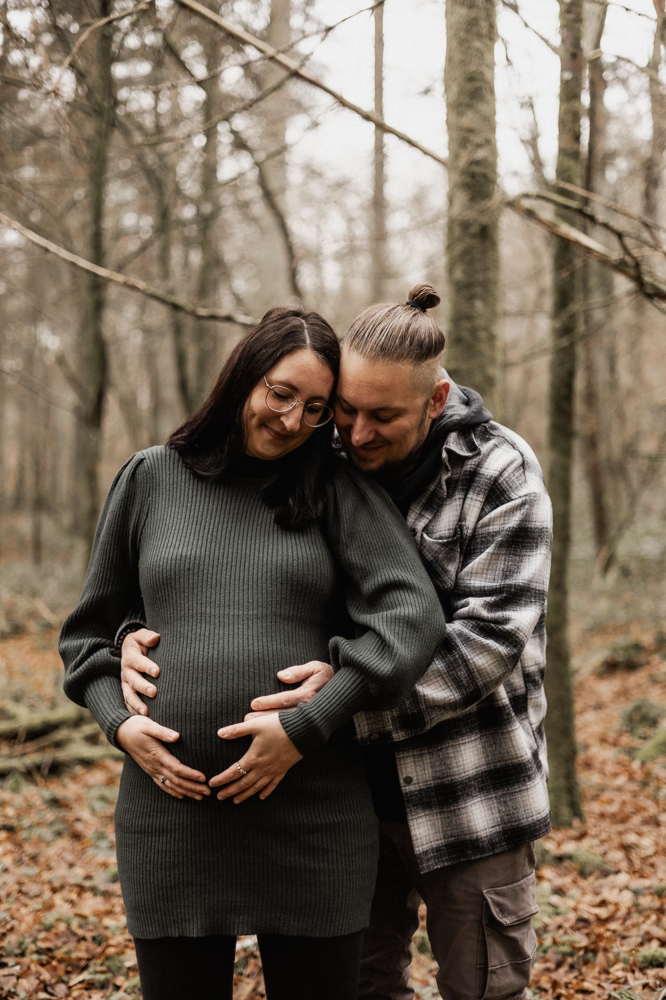 Ein inniges Paar teilt eine Umarmung und hält zärtlich den Babybauch inmitten eines nebligen Herbstwaldes in Konz.