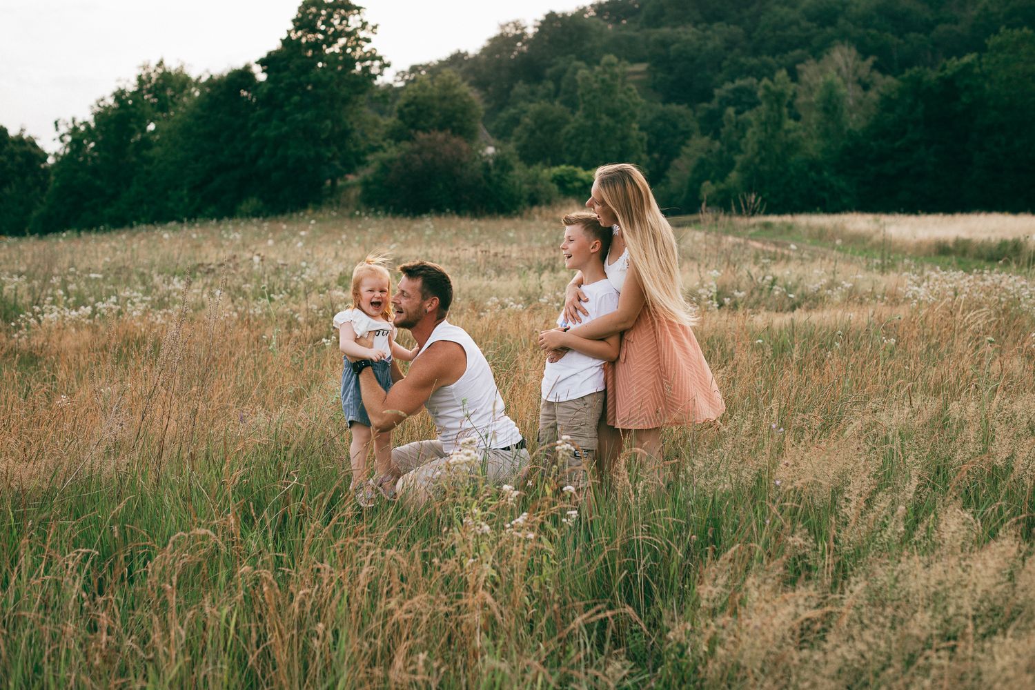 Eine liebevolle Familienszene entfaltet sich in einer Wiese mit hohem Gras während der goldenen Stunde.