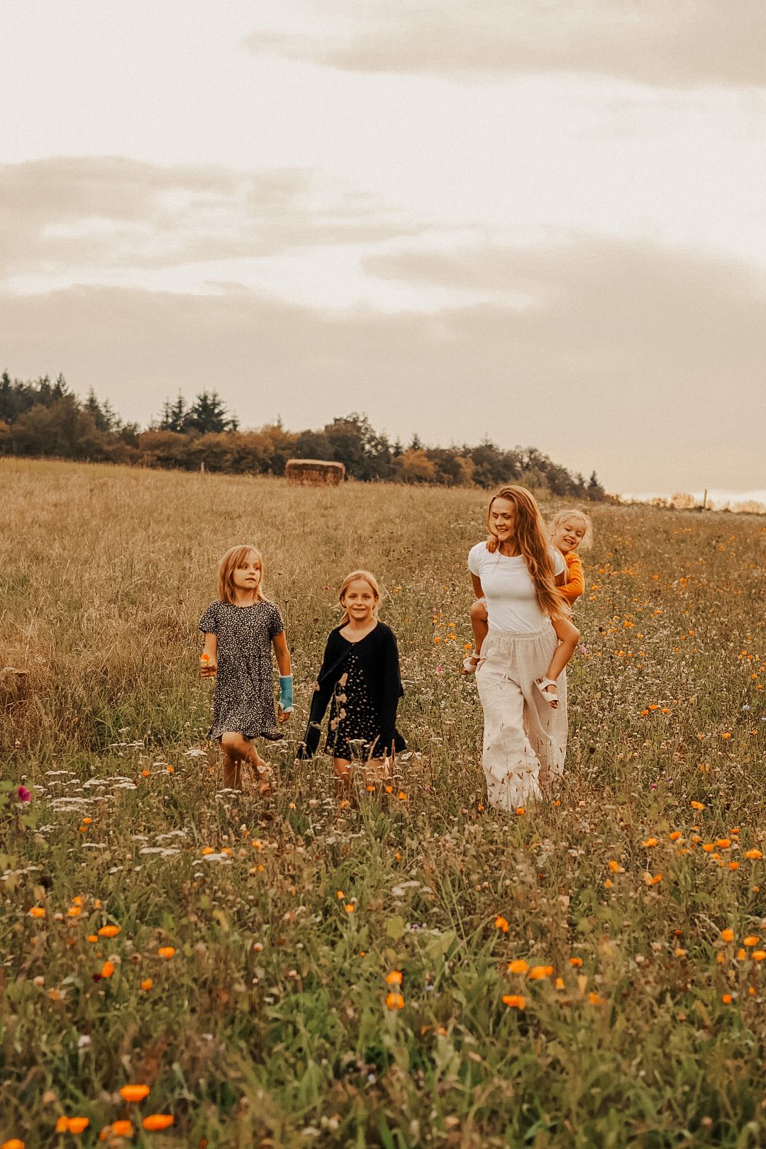 A joyful group laughs and plays together in a field of blooming wildflowers at sunset.