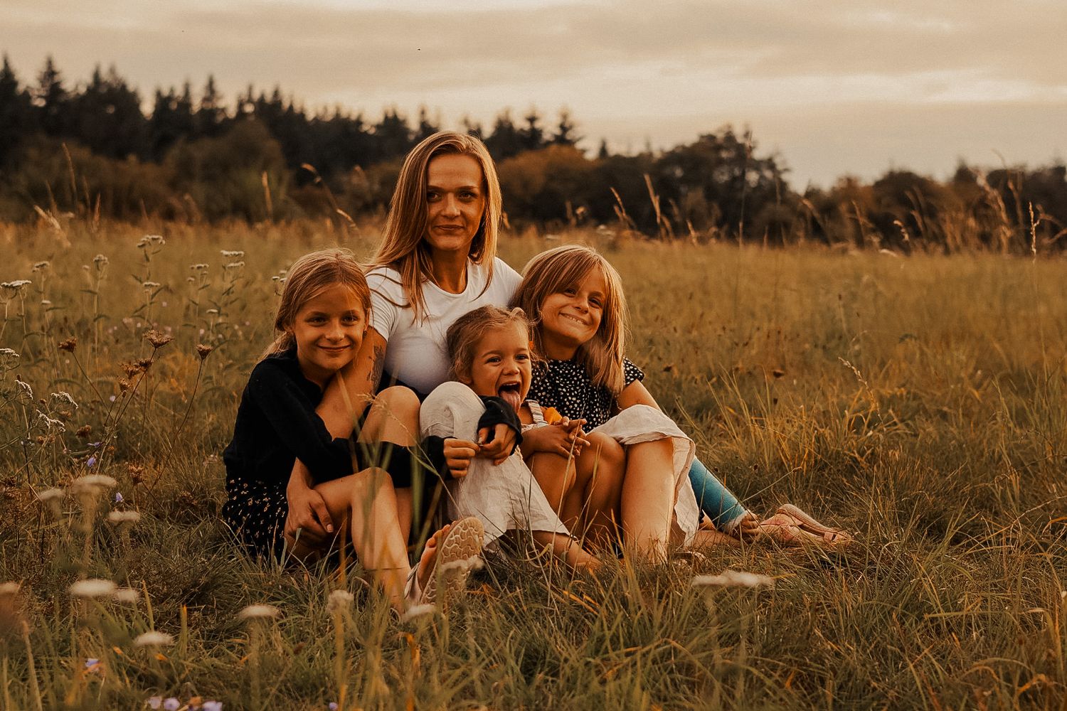Friends sit together and laugh in a golden field during sunset.