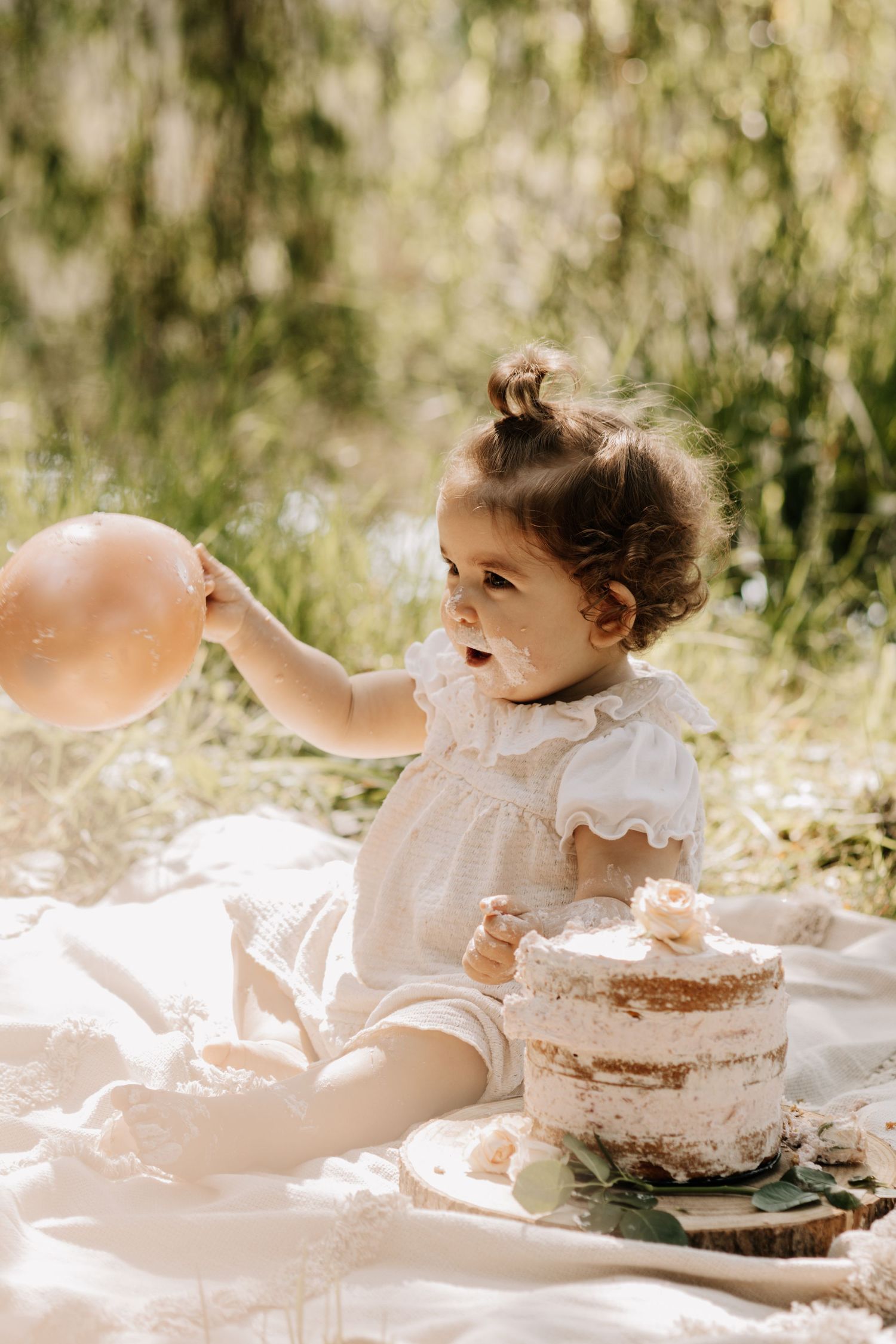 Sweet celebration scene with cake and balloon on picnic blanket in sunlit setting.