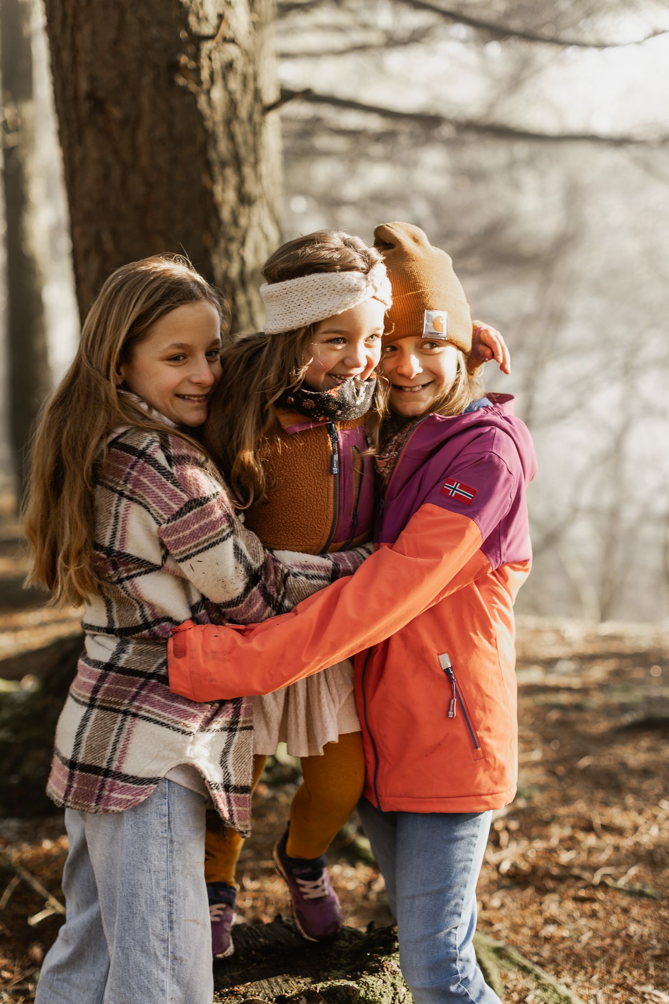 Kinder tollen und umarmen sich in einem winterlichen Wald, umgeben von Laub auf dem Boden in Pellingen.