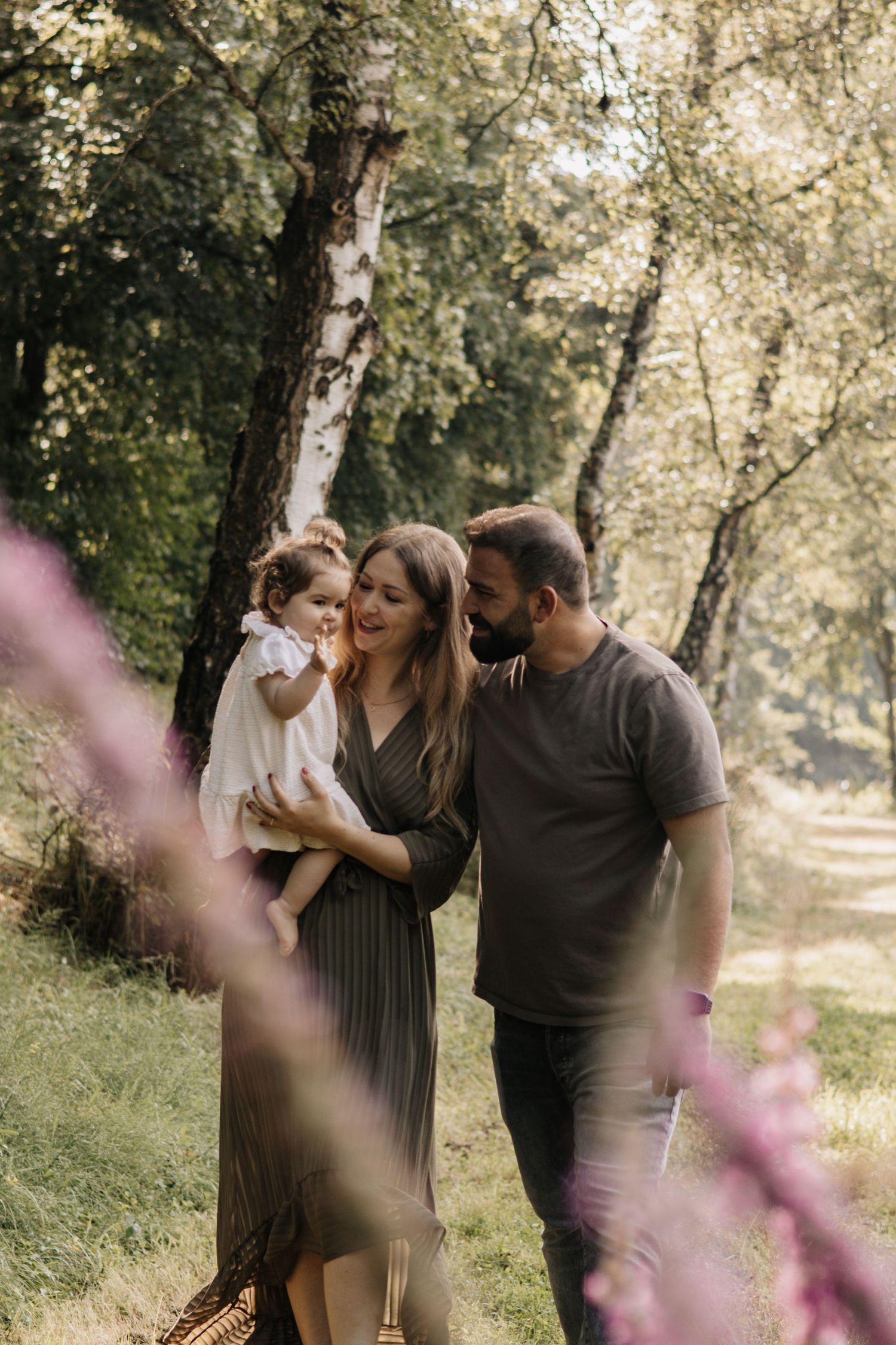 A tranquil family moment captured in a sunlit forest with trees and purple flowers.
