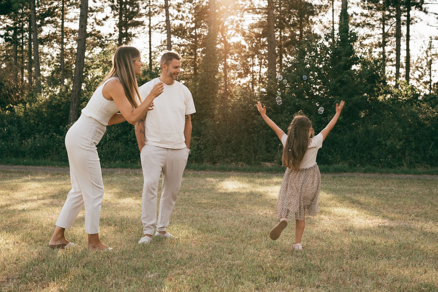Eine Familie spielt und tanzt miteinander auf einer von der Abendsonne erleuchteten Wiese.