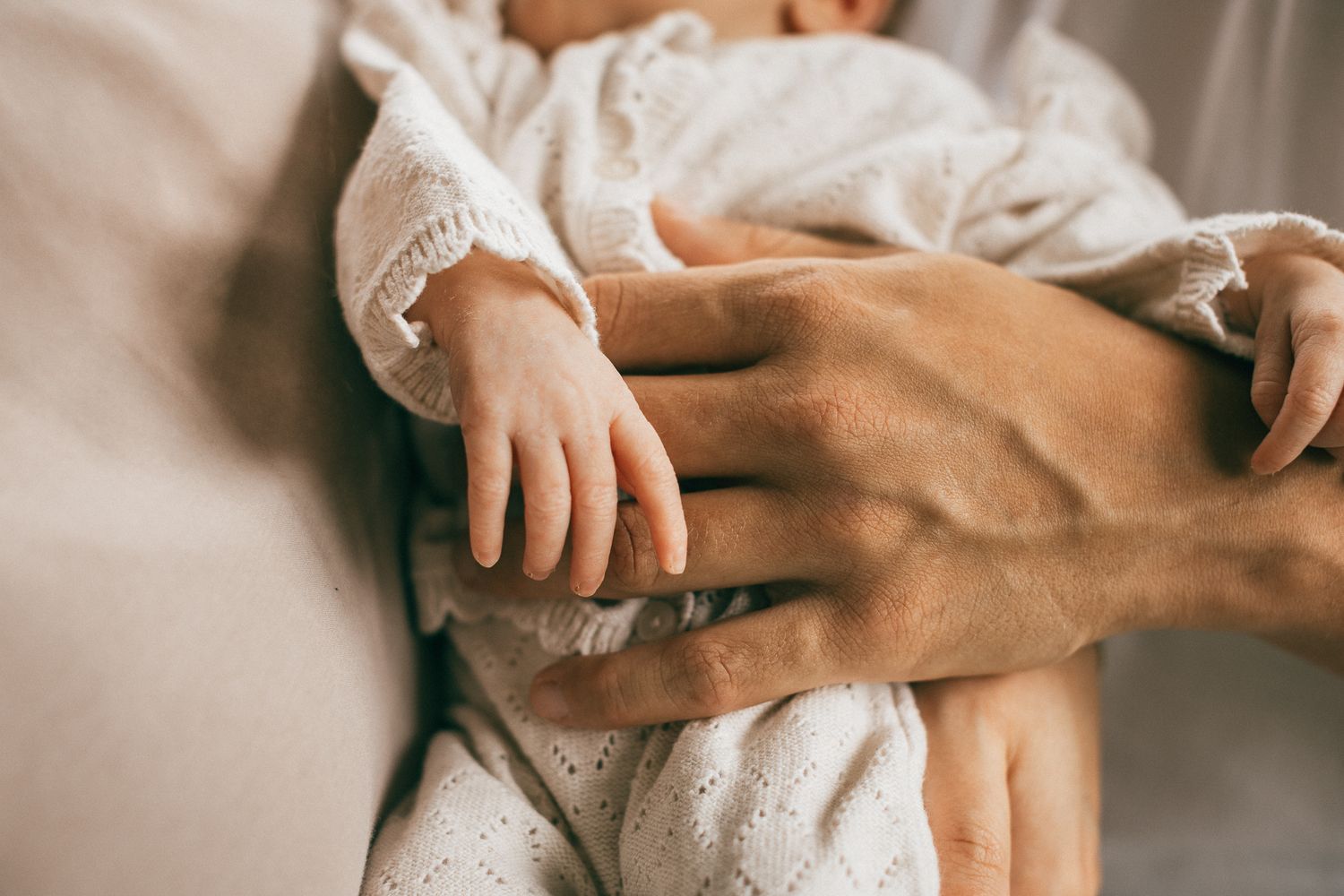 Behutsame Hände halten und liebkosen ein in weißen Stoff gewickeltes Baby in Trier.