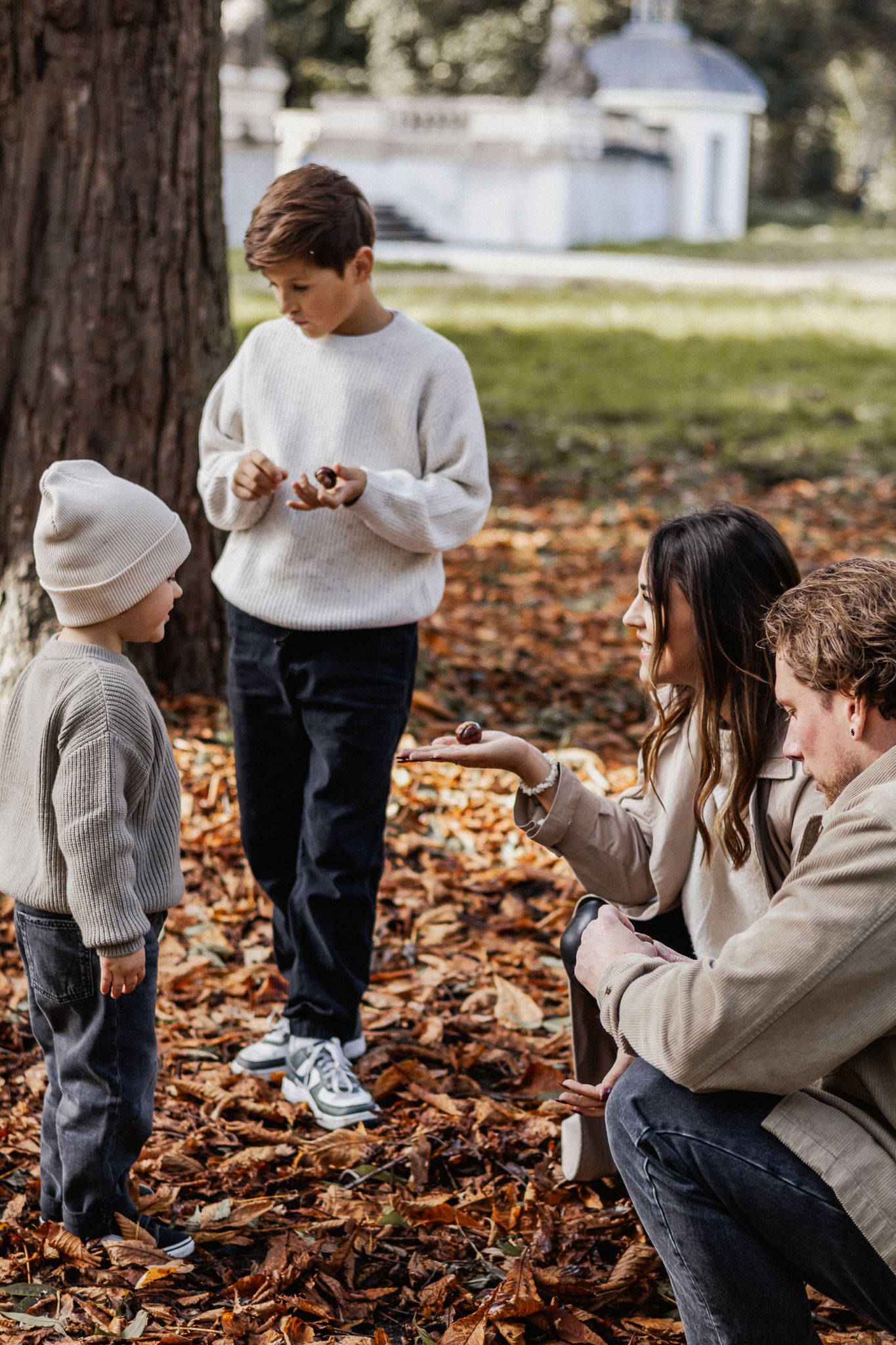 Familie spaziert gemeinsam durch einen Park, bedeckt mit gefallenem Herbstlaub und den letzten Sonnenstrahlen in Trier.
