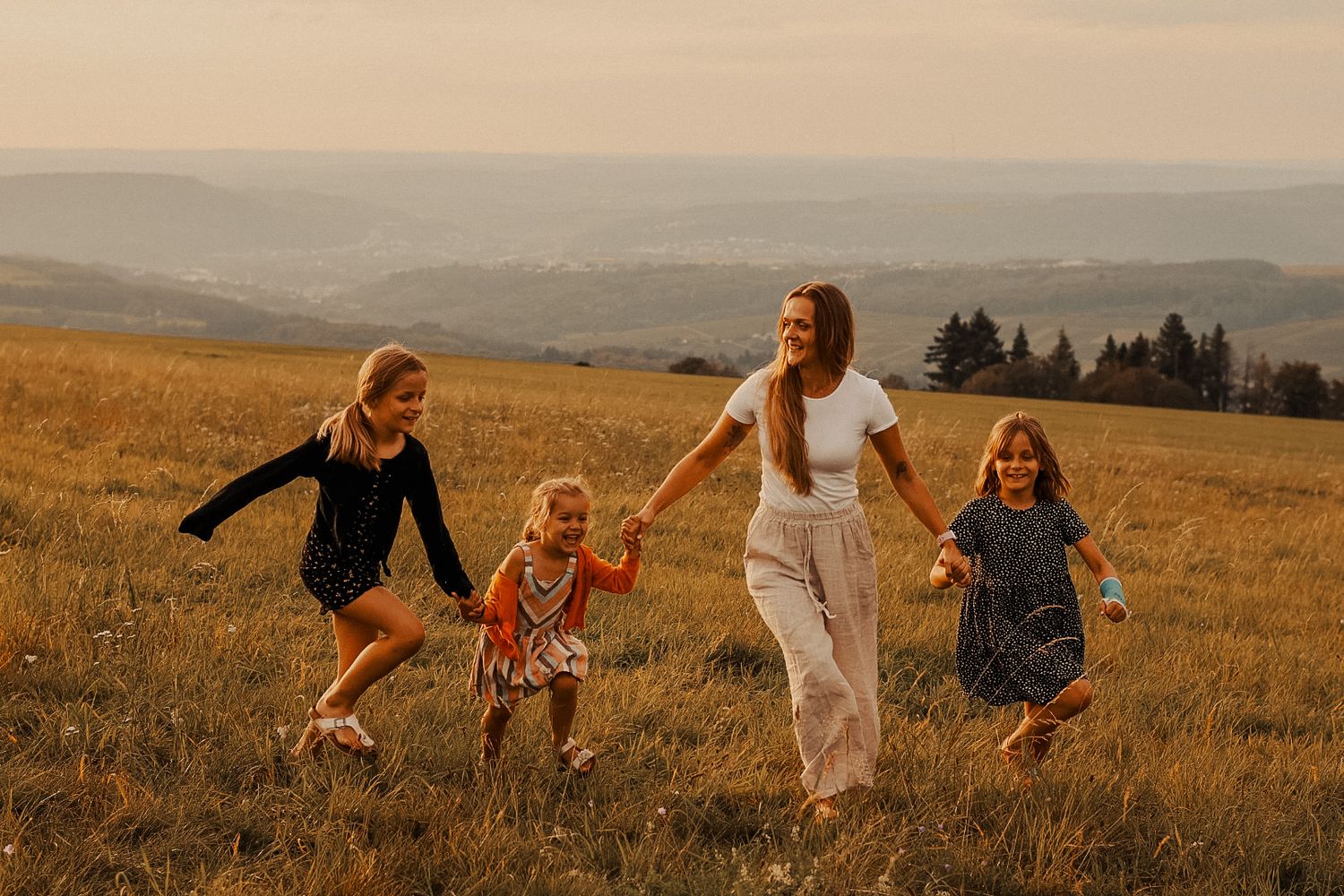 Joyful group running together through sun-drenched mountain meadow at golden hour.