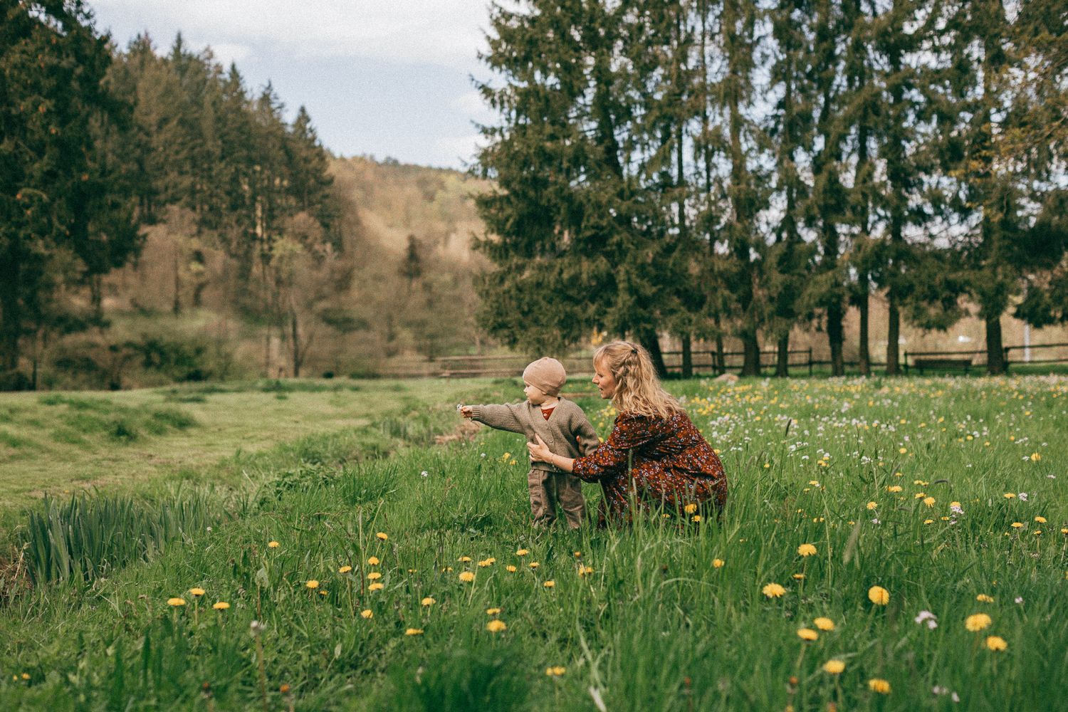 Eine ländliche Mutter Sohn Foto mit hohen Nadelbäumen und blühenden Wildblumenwiesen, beleuchtet vom sanften Licht der Natur in Naurath.