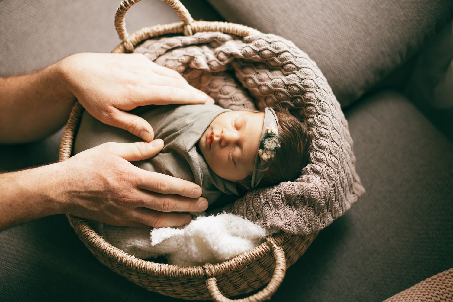 Ein neugeborenes Baby, eingehüllt in ein weiches braunes Tuch, wird sanft von liebevollen Händen seines Papa gehalten.“