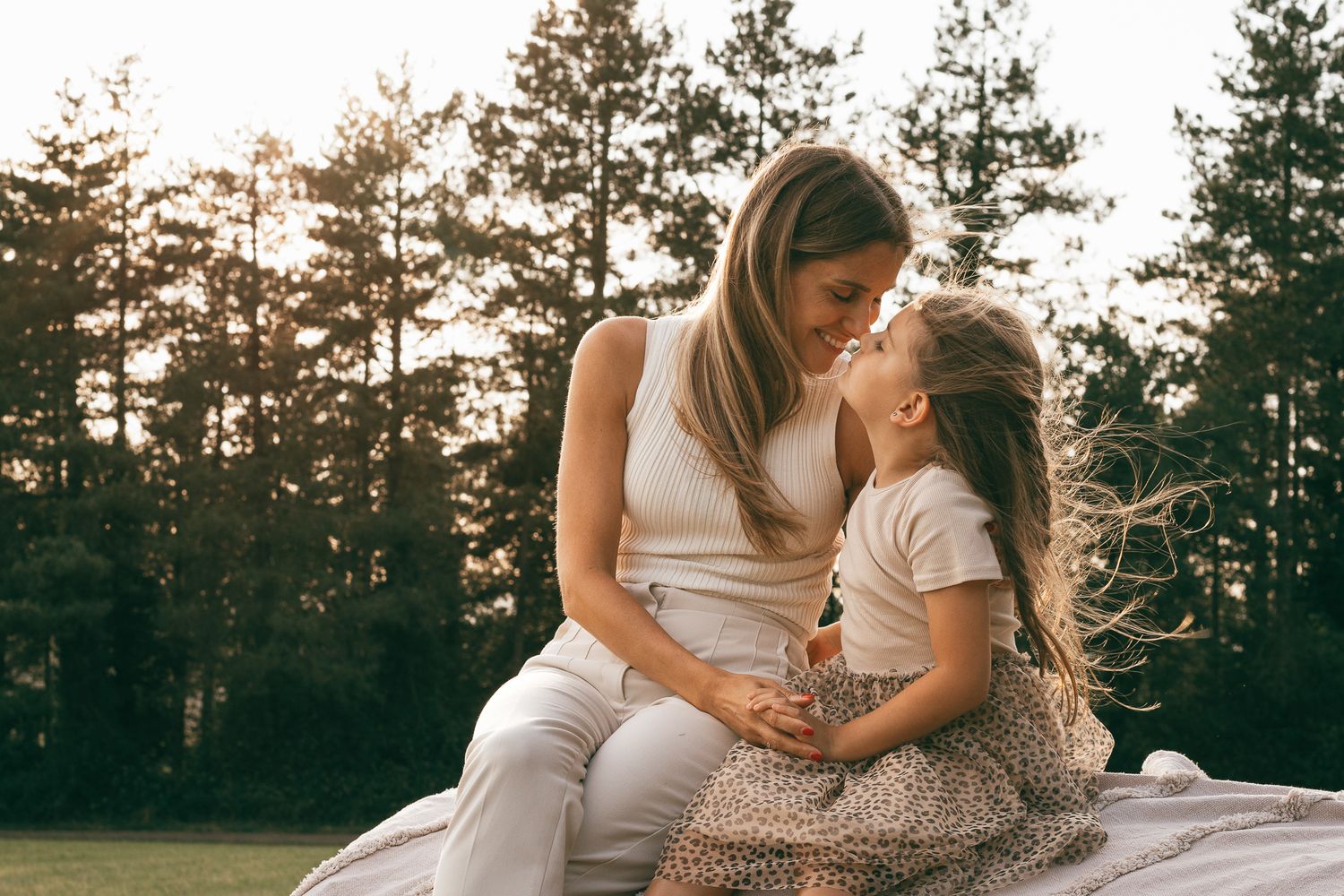 Mutter und Tochter teilen einen innigen Moment vor Kiefern im Licht des Sonnenuntergangs.