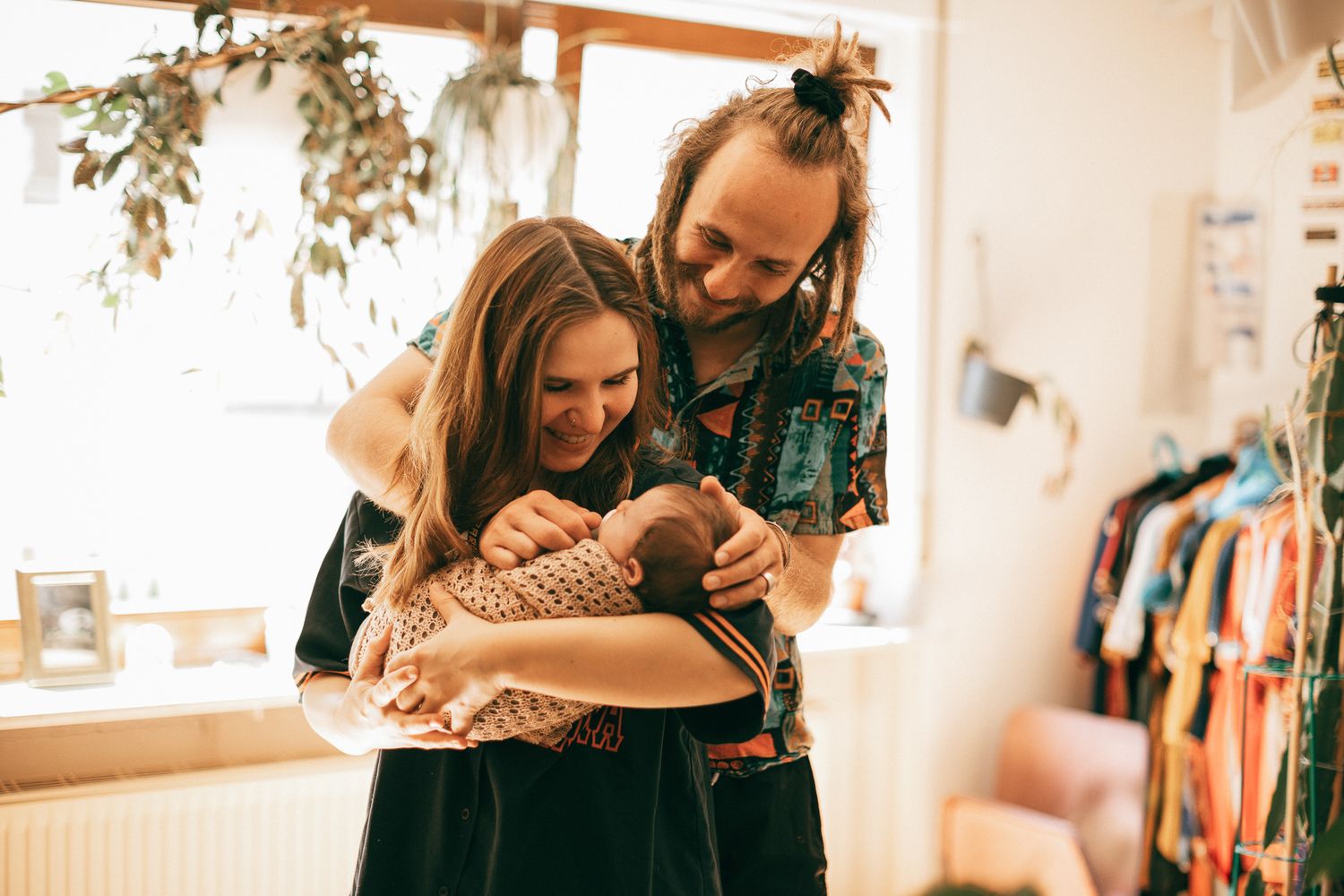 Ein liebevoller Familienmoment im warmen Licht eines Innenraums, vor dem Hintergrund hängender Pflanzen.