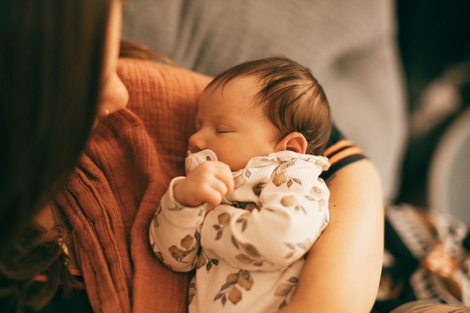 Ein schlafendes Baby, behutsam in eine gemusterte Wickeldecke gehüllt, ruht gemütlich in Mamas Armen.