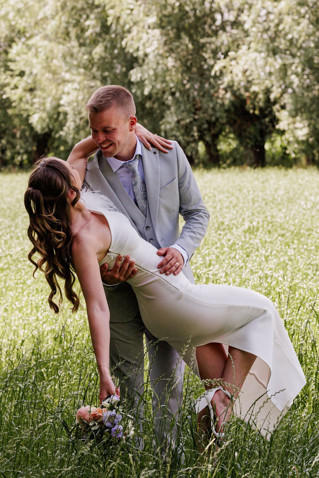 A couple embracing in a field of tall grass and flowers on a sunny day.