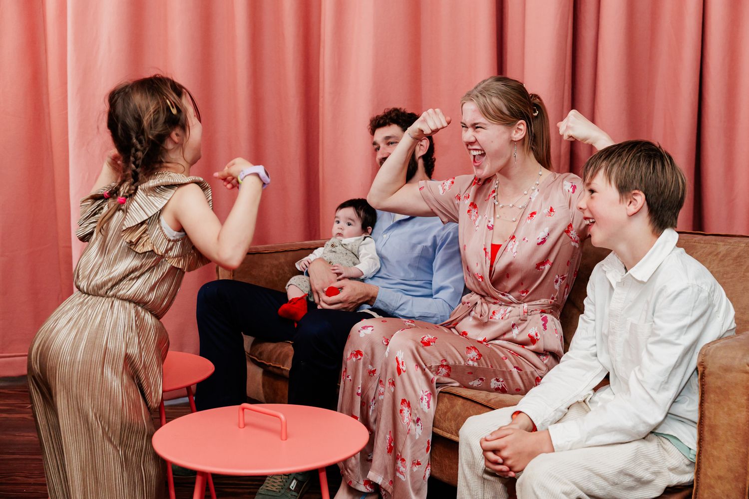 A group of people, including a woman and children, sitting together in a room with a pink curtain backdrop.