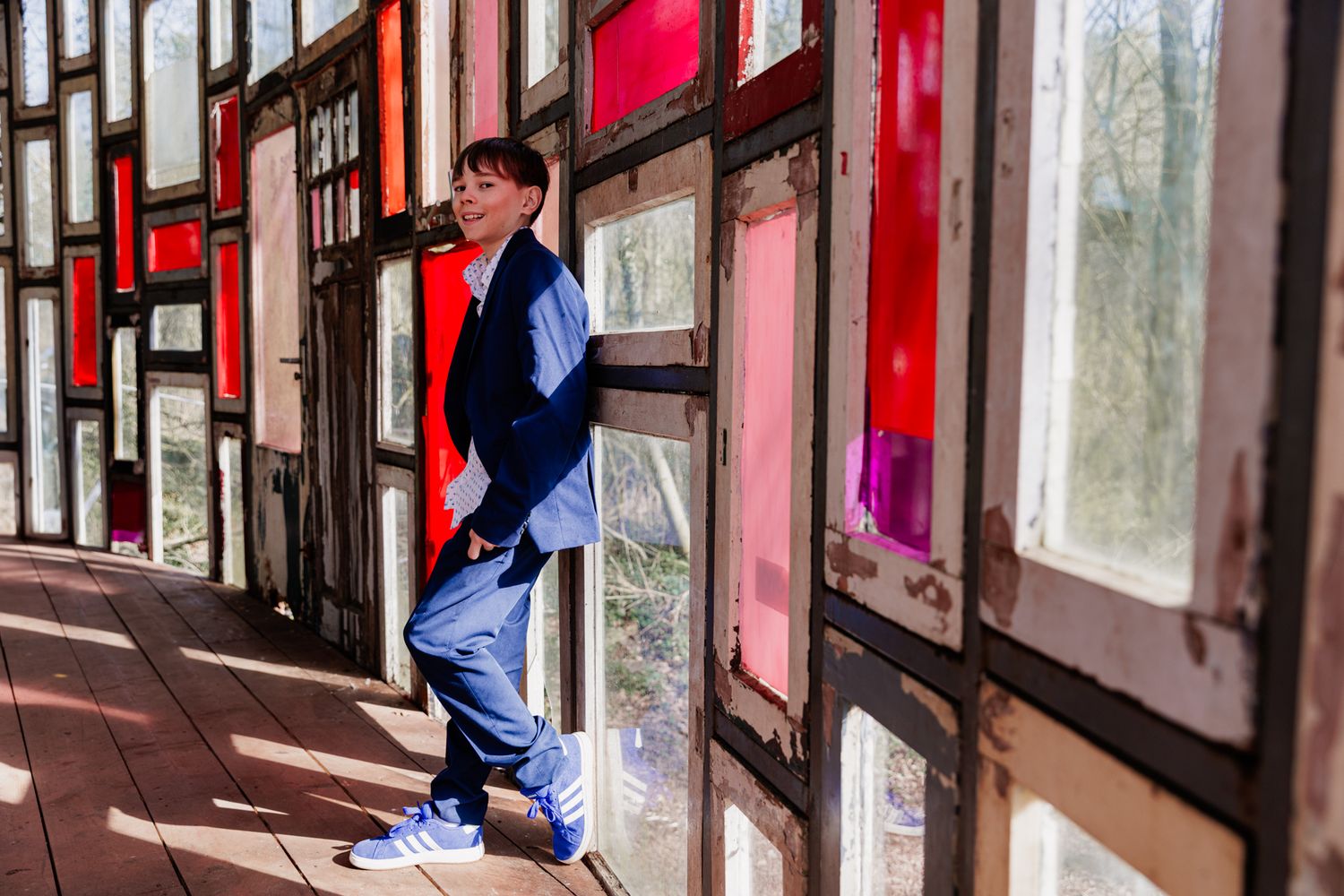 A young man in a blue jacket stands in a doorway with red-framed windows.