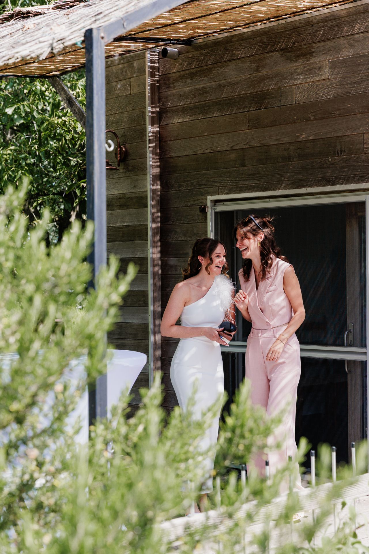 Two women in dresses standing on a wooden porch in a rural setting.