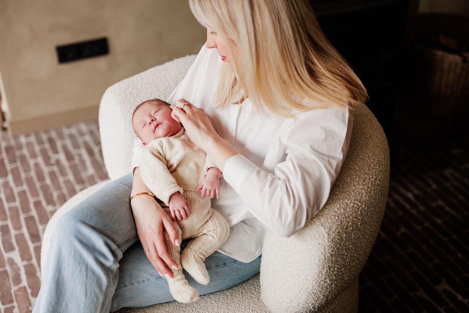 A woman holds a newborn baby in her arms, gazing down at the infant with tenderness.