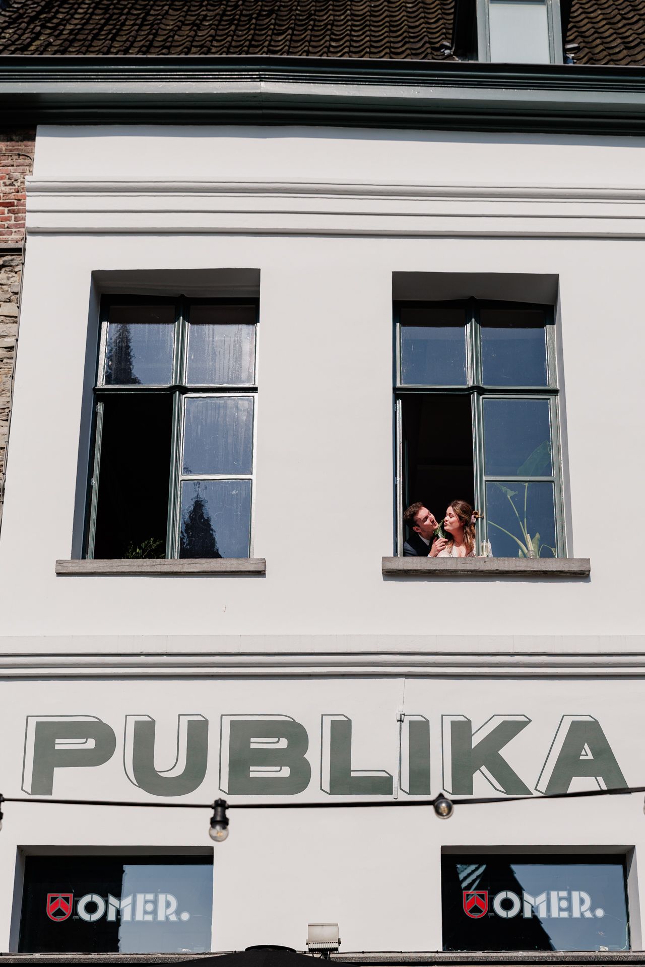 A brick building with the word 'PUBLIKA' displayed prominently, and two people visible in the windows.