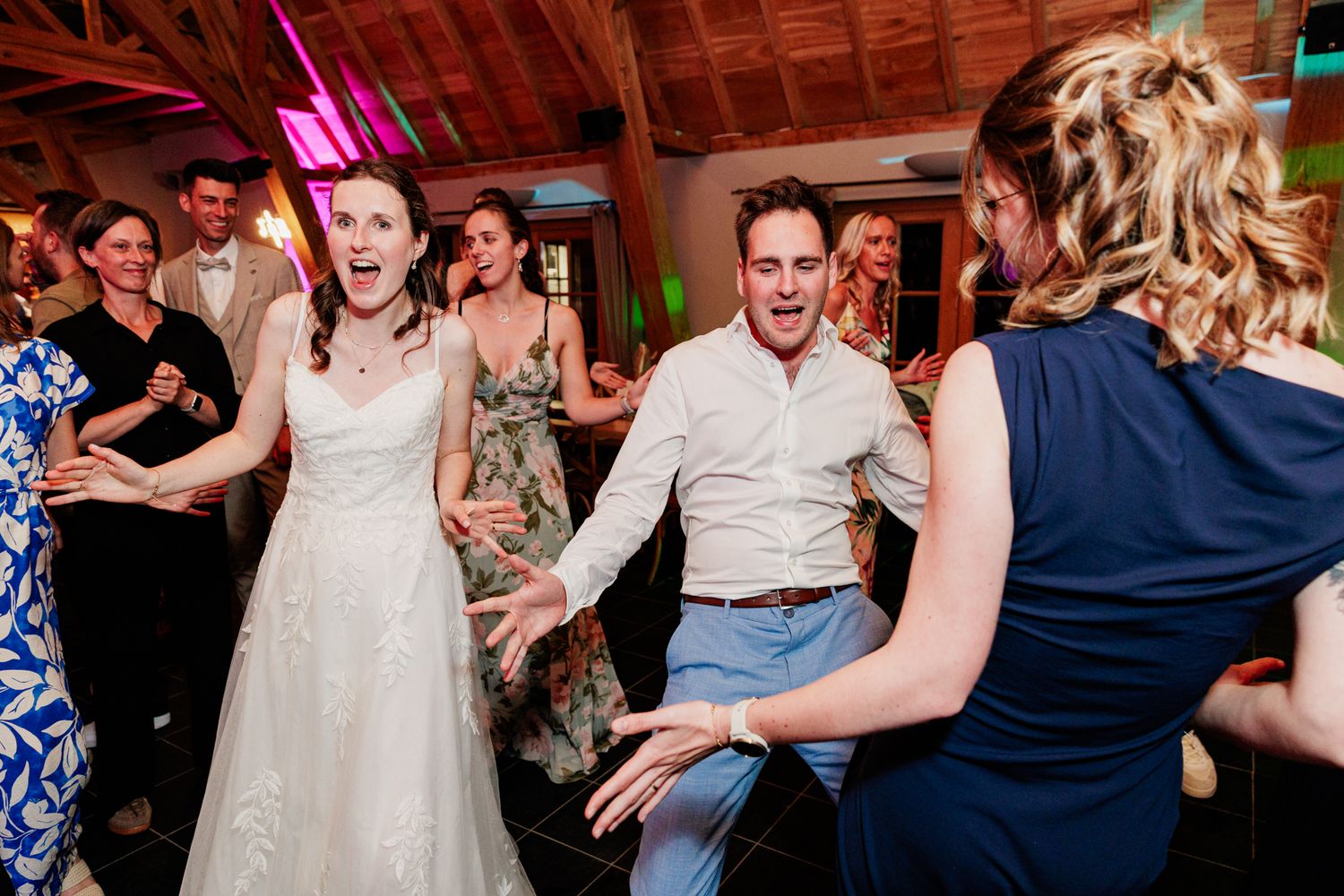 A wedding reception scene showing a bride and groom dancing with guests in a rustic setting.
