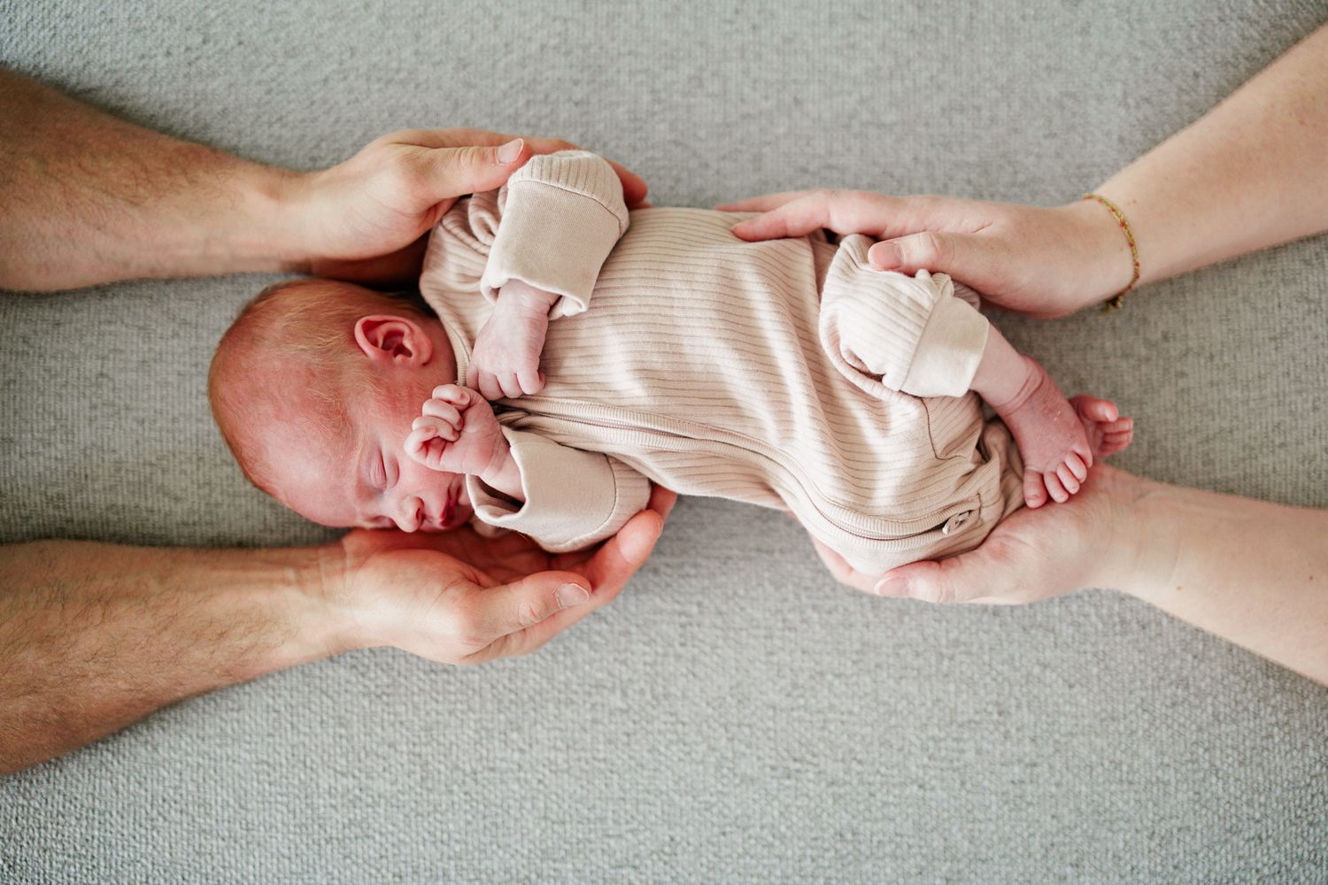 A newborn baby being held gently in the hands of an adult, wrapped in a soft pink blanket.