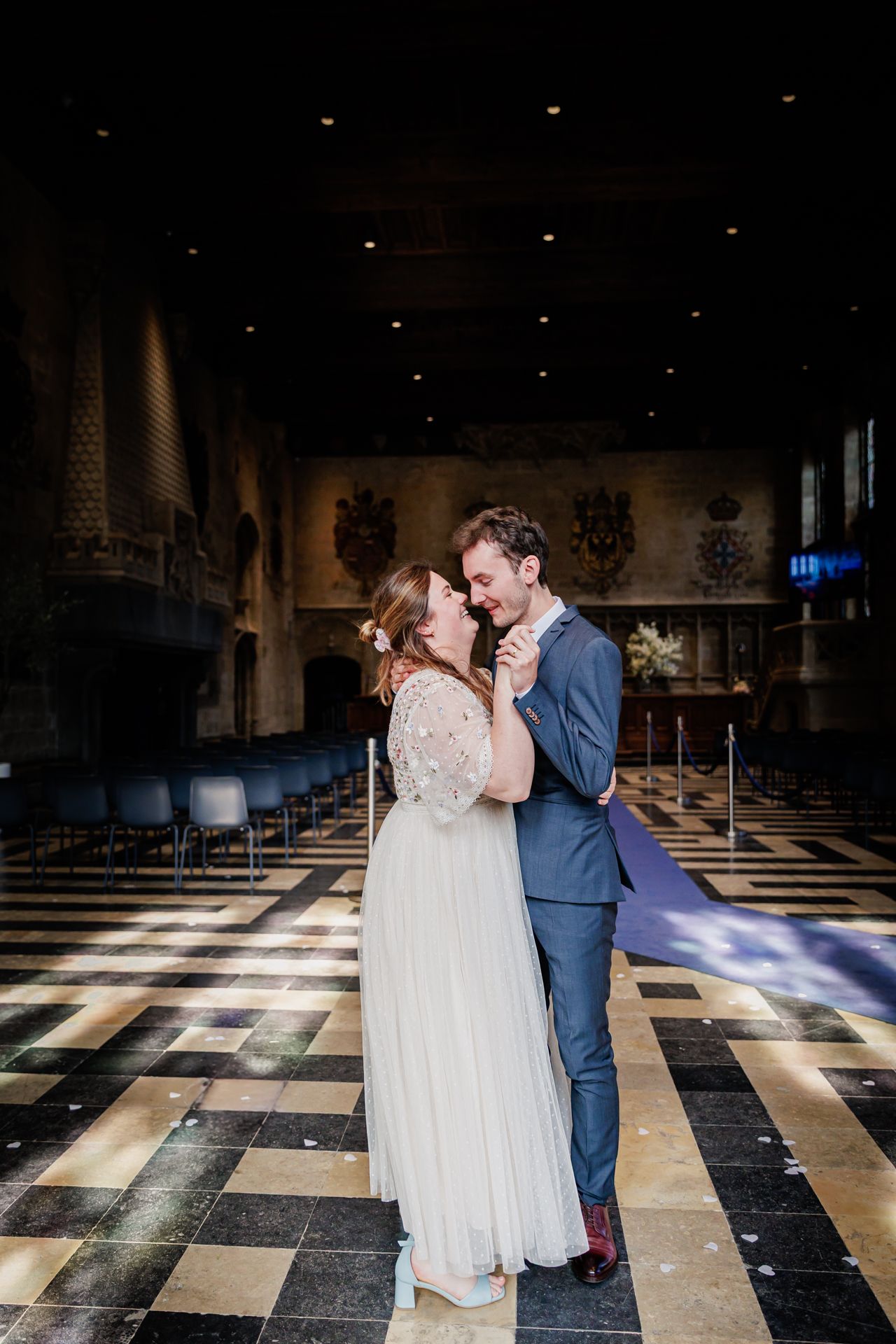 A couple dressed in formal attire embracing and dancing on a checkered floor in a dimly lit room.