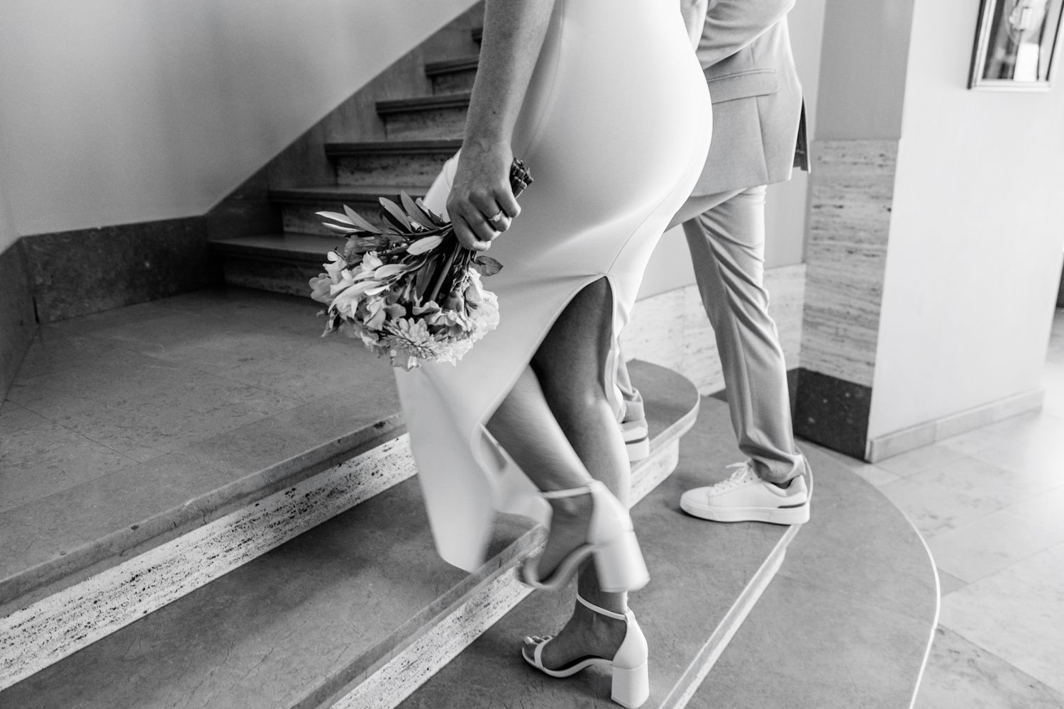 A black and white image showing the lower body of a person holding a bouquet of flowers while standing on stairs.